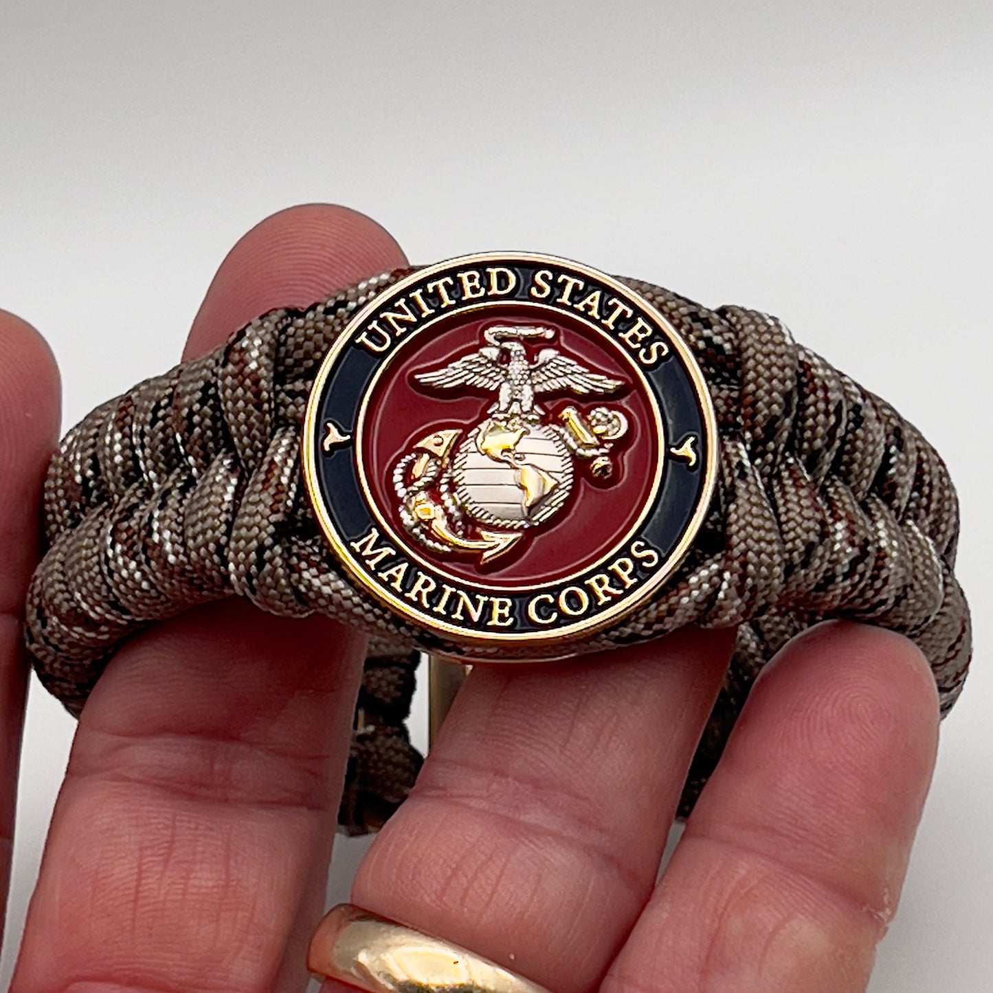 Thick and comfortable braided United States Marine Corps bracelet featuring a 24K gold and silver plated USMC officer Eagle Globe and Anchor medallion, a Cobra style tactical buckle and woven with Desert Camo paracord.