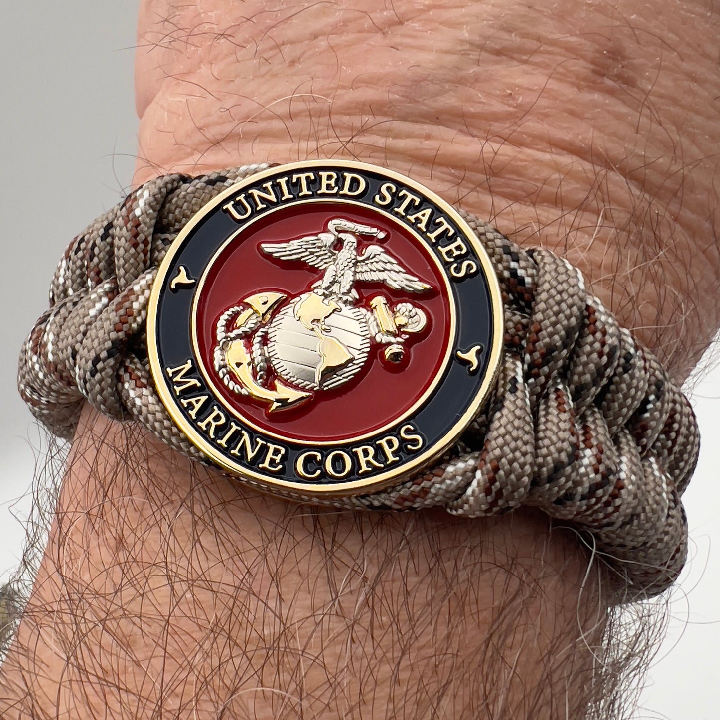 Thick and comfortable braided United States Marine Corps bracelet featuring a 24K gold and silver plated USMC officer Eagle Globe and Anchor medallion, a Cobra style tactical buckle and woven with Desert Camo paracord.