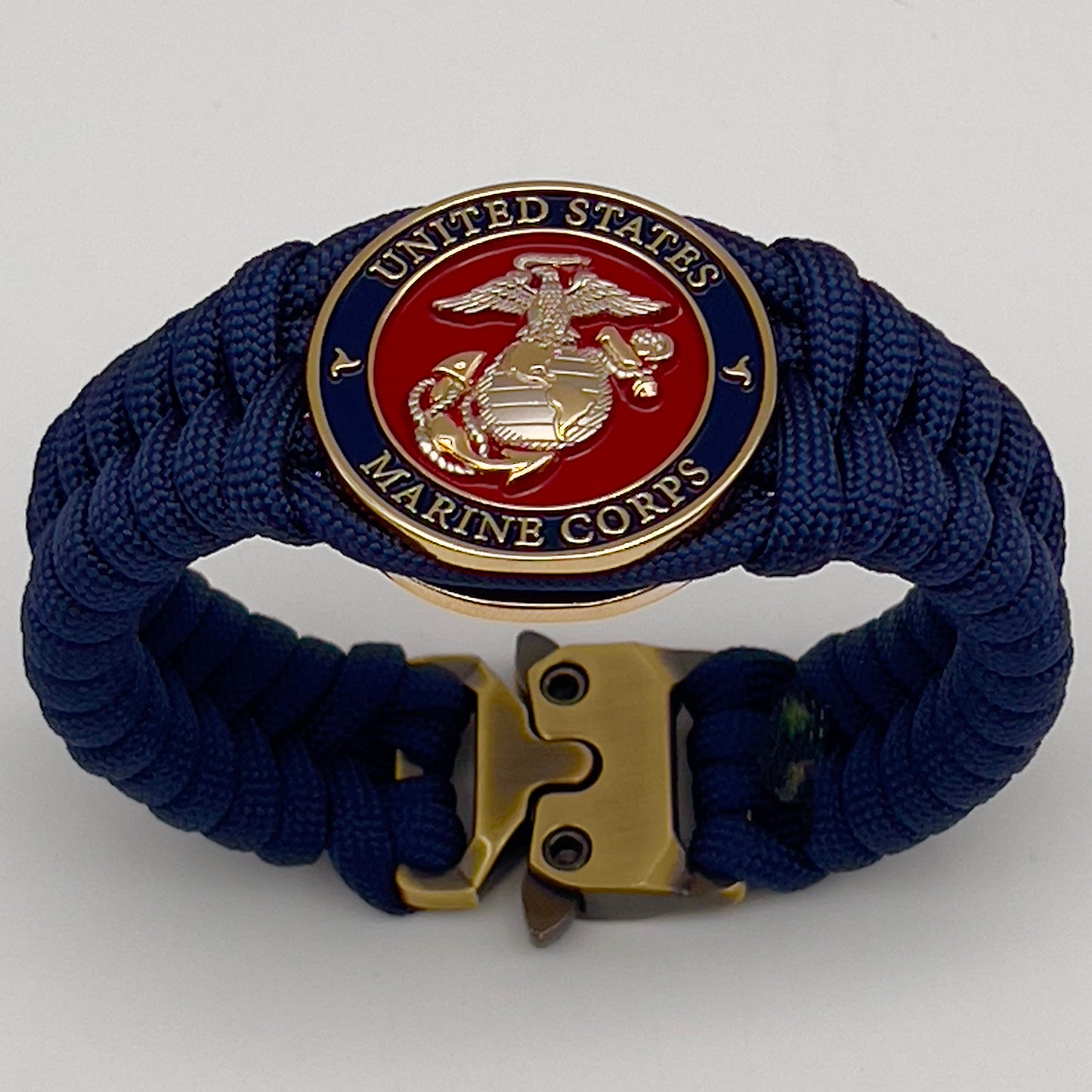 Thick and comfortable braided United States Marine Corps bracelet featuring a 24K gold and silver plated USMC officer Eagle Globe and Anchor medallion, a Cobra style tactical buckle and woven with Navy blue paracord.