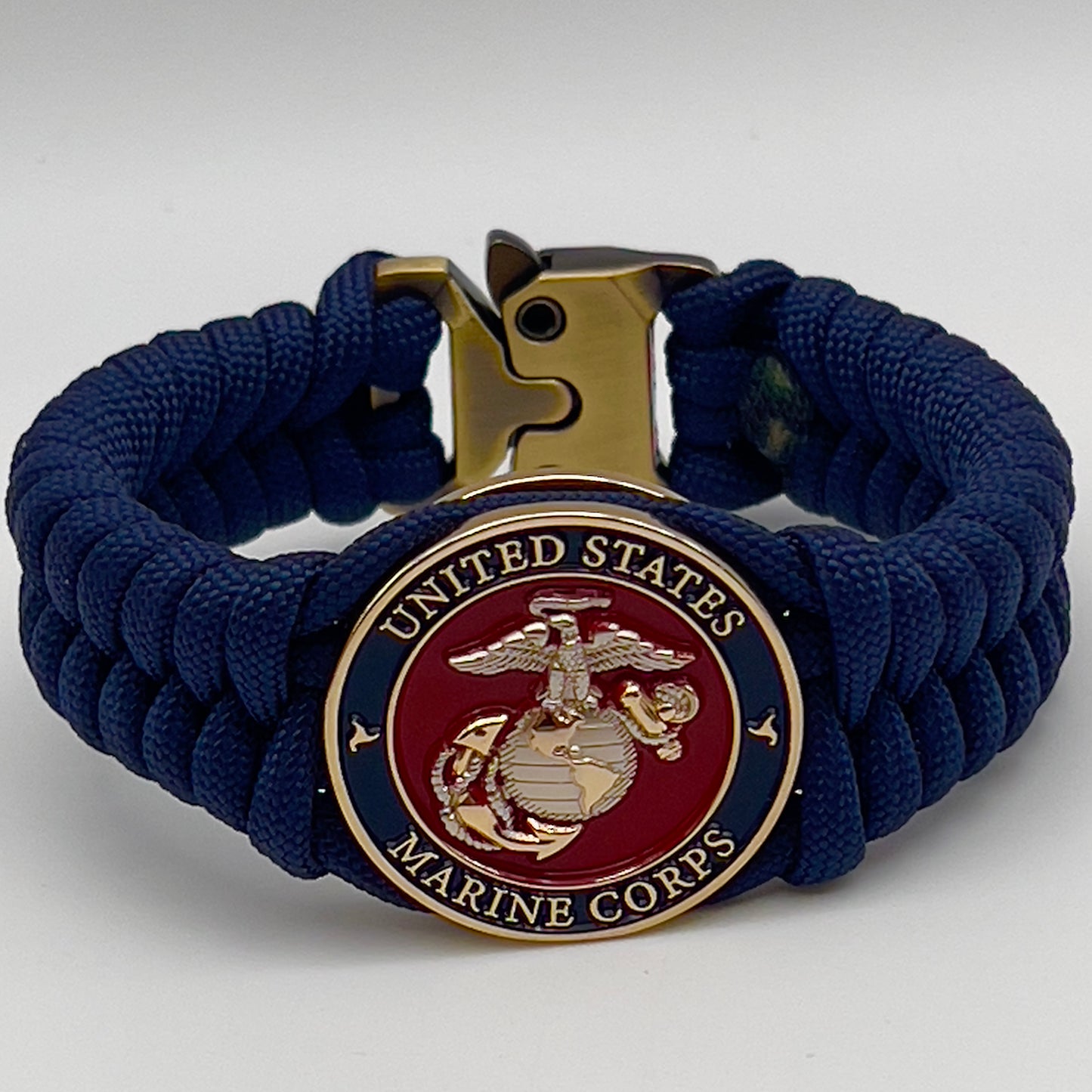 Thick and comfortable braided United States Marine Corps bracelet featuring a 24K gold and silver plated USMC officer Eagle Globe and Anchor medallion, a Cobra style tactical buckle and woven with Navy blue paracord.