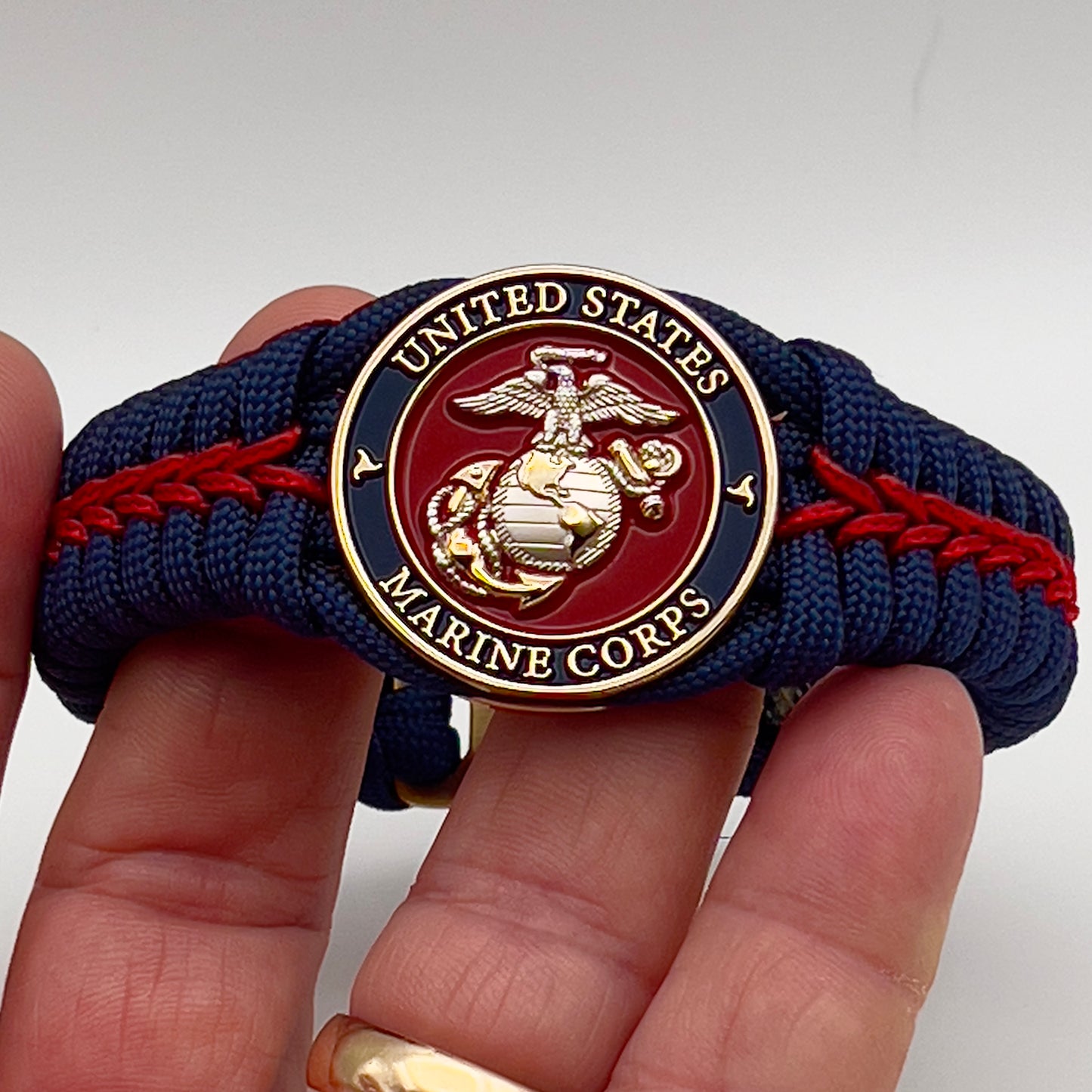 Thick and comfortable braided United States Marine Corps bracelet featuring a 24K gold and silver plated USMC officer Eagle Globe and Anchor medallion, a Cobra style tactical buckle and woven with Navy blue and Imperial red paracord.