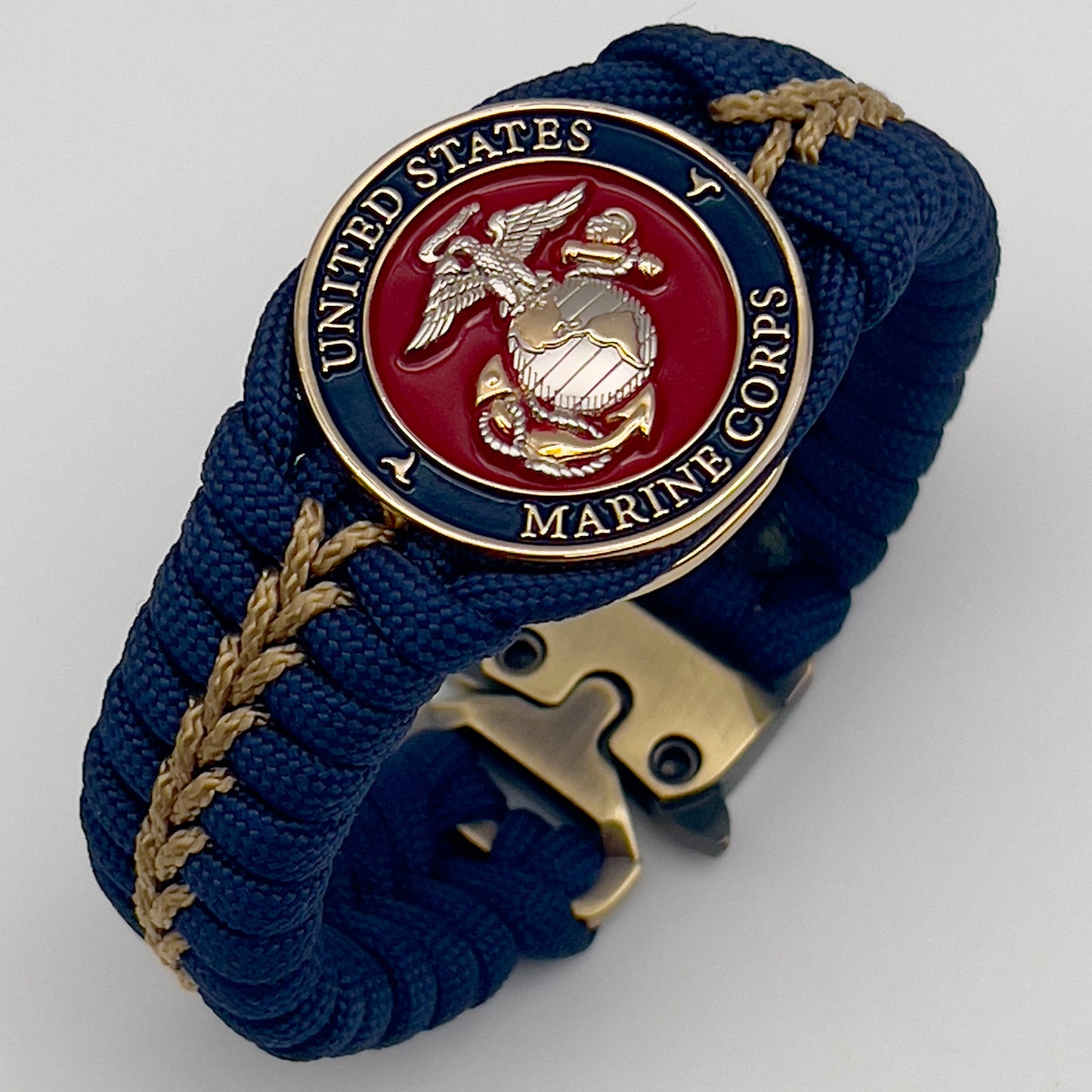 Thick and comfortable braided United States Marine Corps bracelet featuring a 24K gold and silver plated USMC officer Eagle Globe and Anchor medallion, a Cobra style tactical buckle and woven with Navy blue and gold paracord.