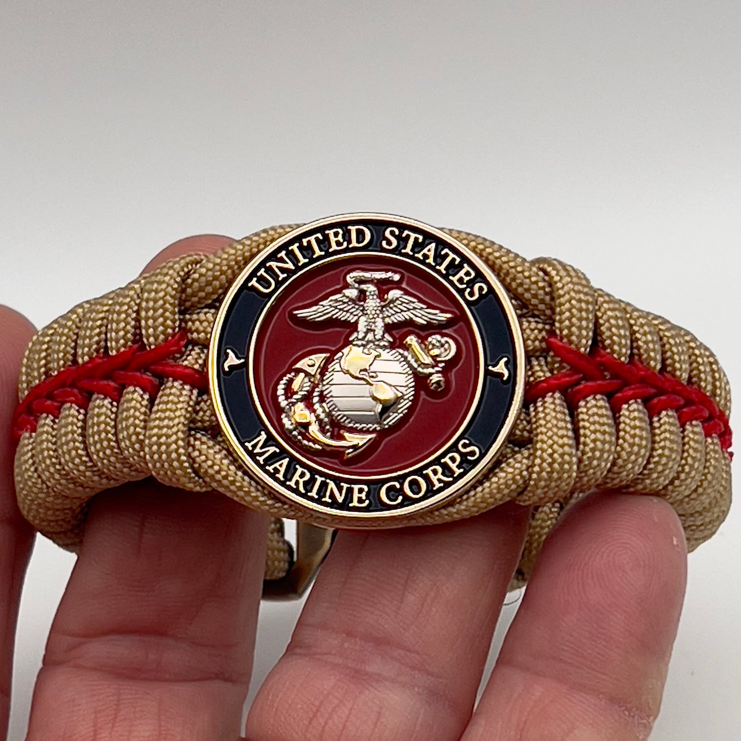 Thick and comfortable braided United States Marine Corps bracelet featuring a 24K gold and silver plated USMC officer Eagle Globe and Anchor medallion, a Cobra style tactical buckle and woven with gold 550 and Imperial red micro paracord.