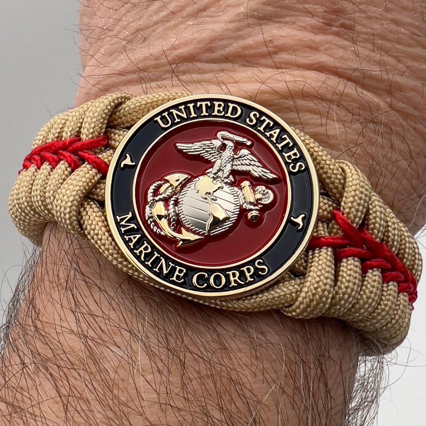 Thick and comfortable braided United States Marine Corps bracelet featuring a 24K gold and silver plated USMC officer Eagle Globe and Anchor medallion, a Cobra style tactical buckle and woven with gold 550 and Imperial red micro paracord.