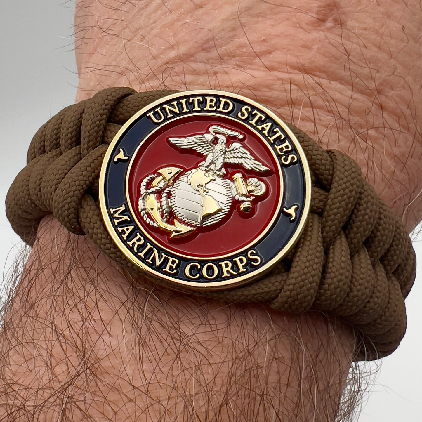 Thick and comfortable braided United States Marine Corps bracelet featuring a 24K gold and silver plated USMC officer Eagle Globe and Anchor medallion, a Cobra style tactical buckle and woven with Coyote brown 550 paracord.