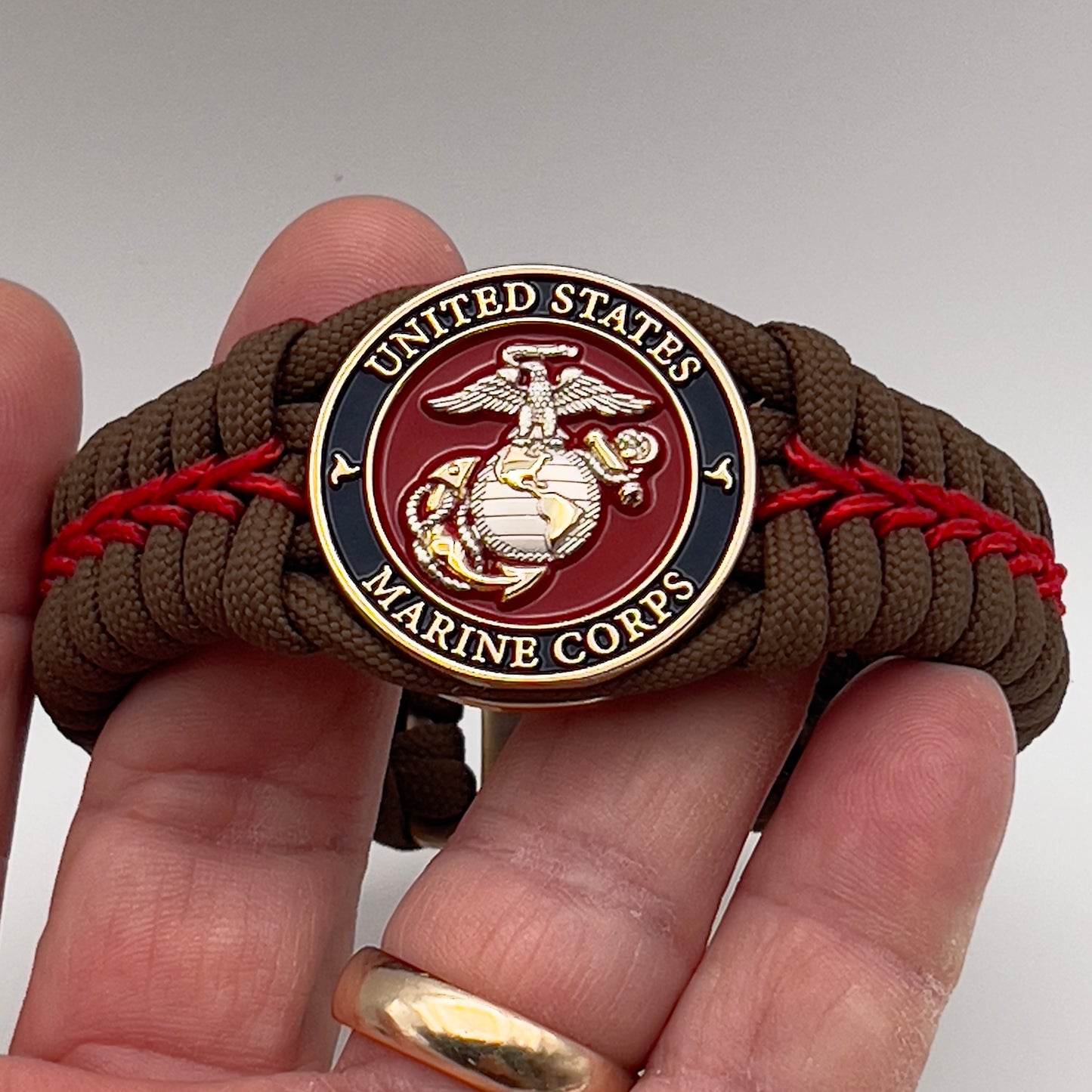Thick, semi-rigid and comfortable braided United States Marine Corps bracelet featuring a 24K gold and silver plated USMC officer Eagle Globe and Anchor medallion, a Cobra style tactical buckle and woven with Coyote brown 550 and Imperial red micro paracord.