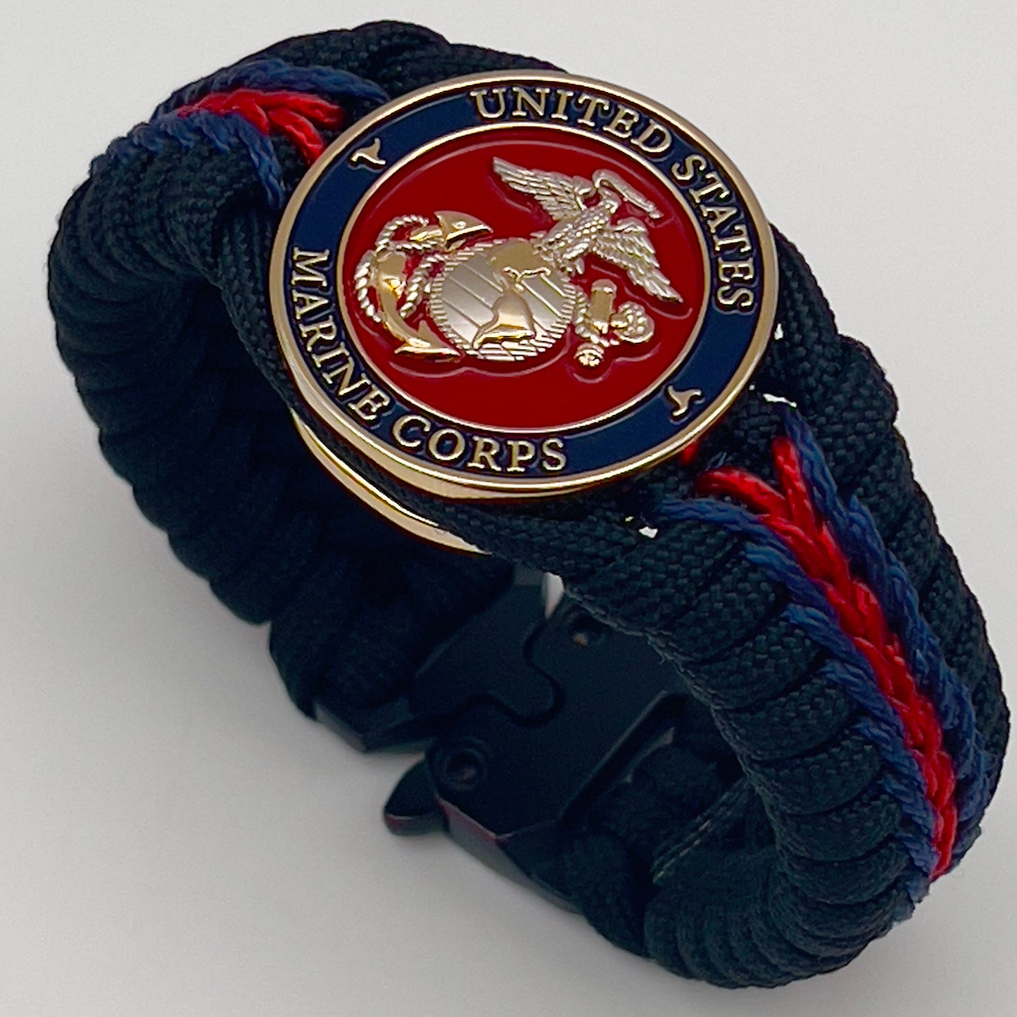 Thick, semi-rigid and comfortable braided United States Marine Corps bracelet featuring a 24K gold and silver plated USMC officer Eagle Globe and Anchor medallion, a black Cobra style tactical buckle and woven with Navy blue, Imperial red and black paracord.