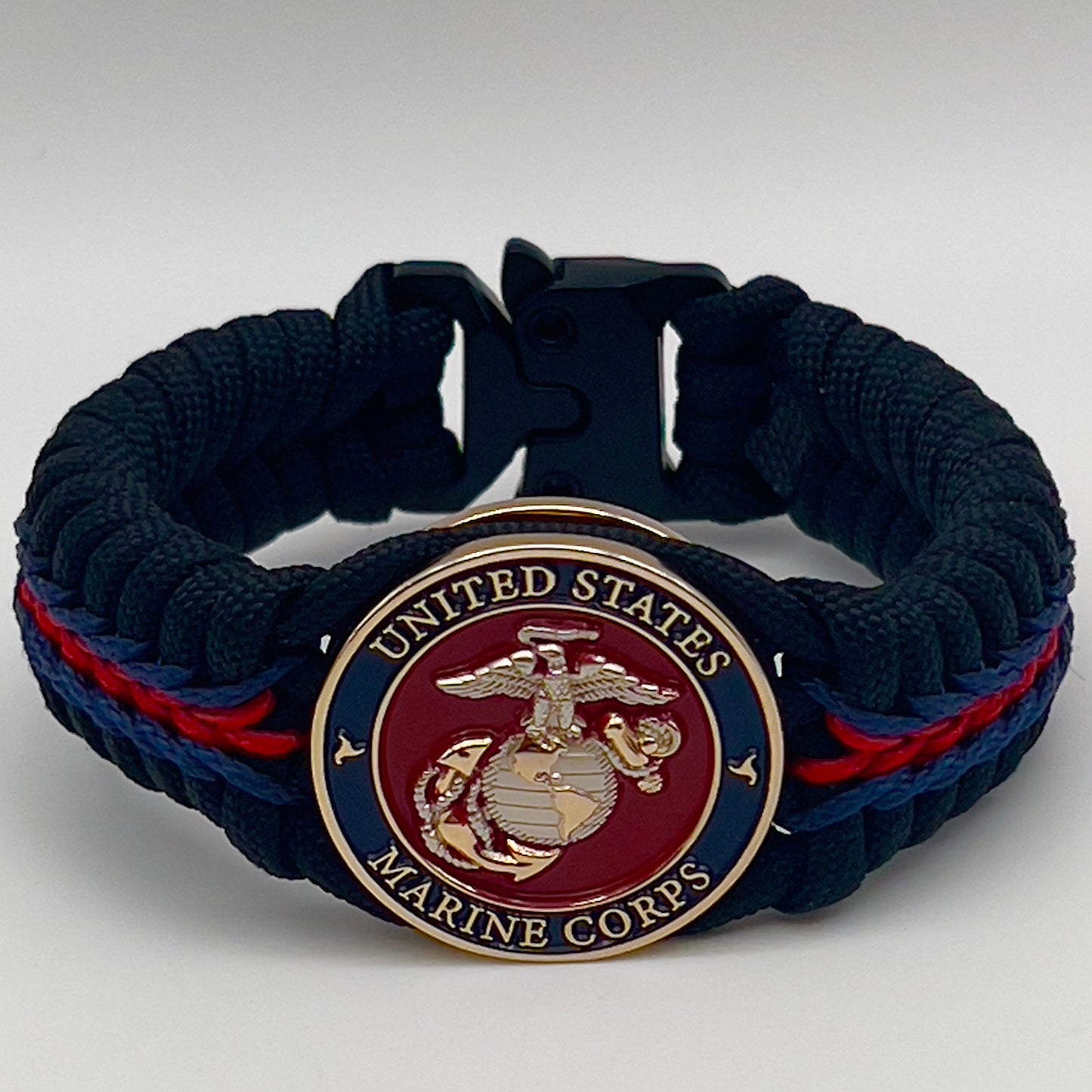 Thick, semi-rigid and comfortable braided United States Marine Corps bracelet featuring a 24K gold and silver plated USMC officer Eagle Globe and Anchor medallion, a black Cobra style tactical buckle and woven with Navy blue, Imperial red and black paracord.