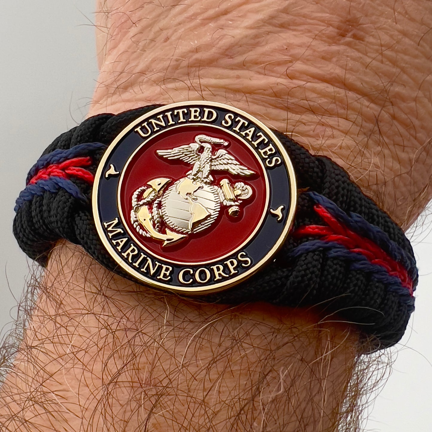 Thick, semi-rigid and comfortable braided United States Marine Corps bracelet featuring a 24K gold and silver plated USMC officer Eagle Globe and Anchor medallion, a black Cobra style tactical buckle and woven with Navy blue, Imperial red and black paracord.