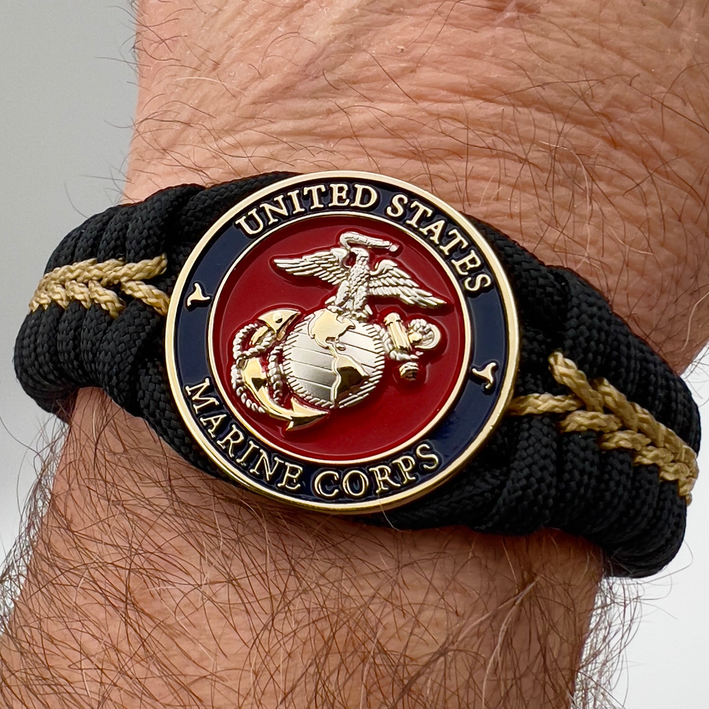 Thick, semi-rigid and comfortable braided United States Marine Corps bracelet featuring a 24K gold and silver plated USMC officer Eagle Globe and Anchor medallion, a black Cobra style tactical buckle and woven with black 550 and gold micro paracord.