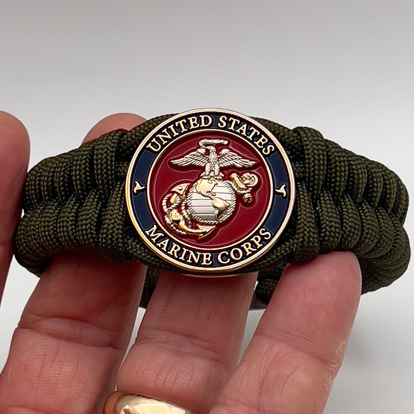 Thick, semi-rigid and comfortable braided United States Marine Corps bracelet featuring a 24K gold and silver plated USMC officer Eagle Globe and Anchor medallion, a gold Cobra style tactical buckle and woven with olive drab 550 paracord.