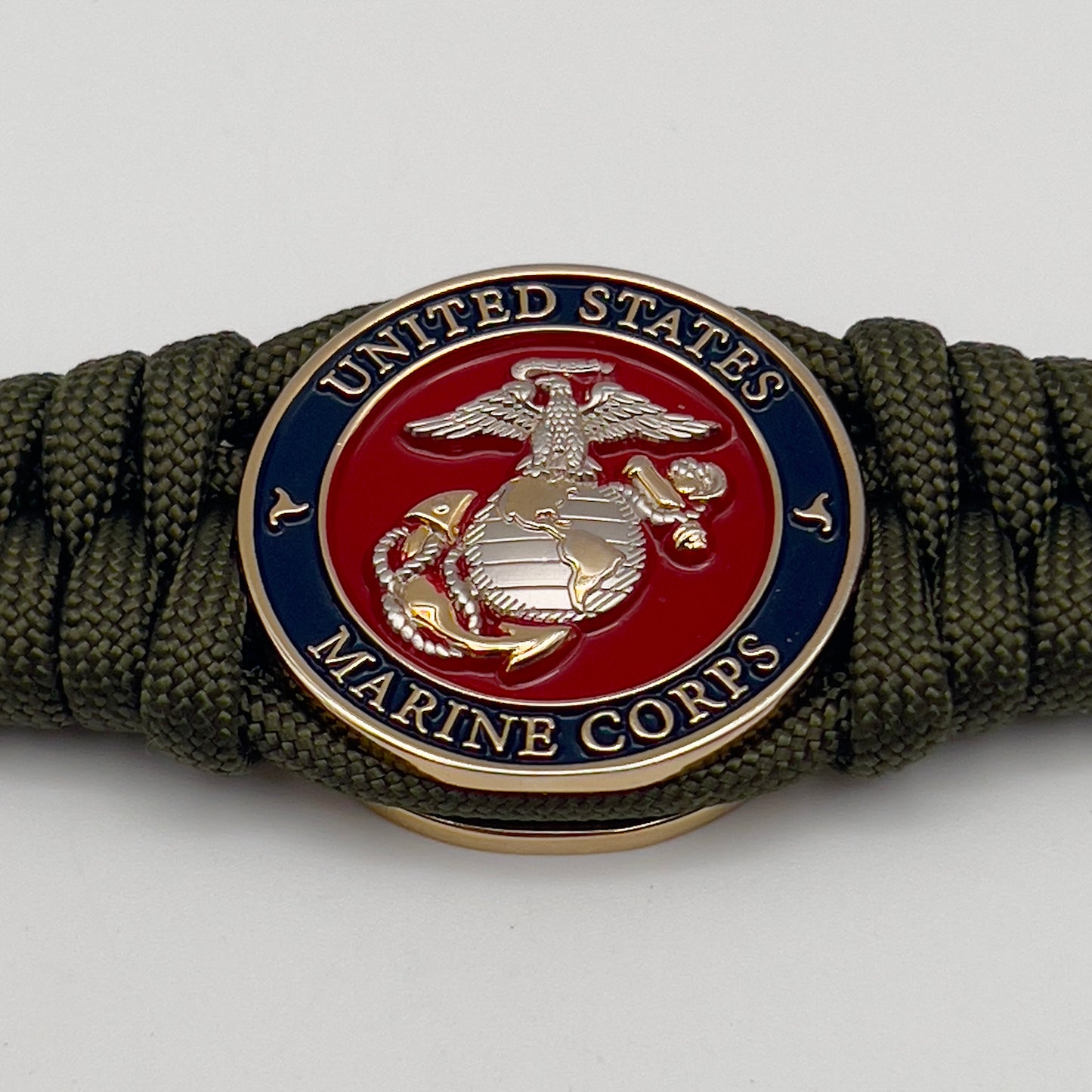 Thick, semi-rigid and comfortable braided United States Marine Corps bracelet featuring a 24K gold and silver plated USMC officer Eagle Globe and Anchor medallion, a gold Cobra style tactical buckle and woven with olive drab 550 paracord.