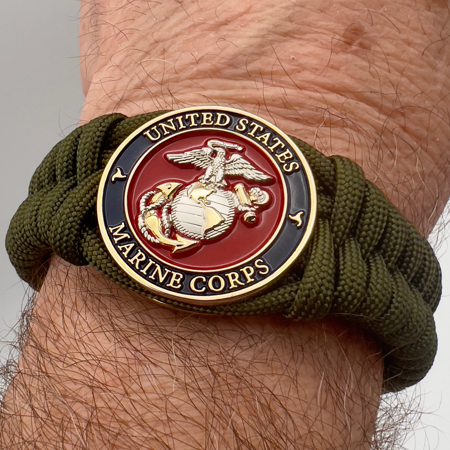 Thick, semi-rigid and comfortable braided United States Marine Corps bracelet featuring a 24K gold and silver plated USMC officer Eagle Globe and Anchor medallion, a gold Cobra style tactical buckle and woven with olive drab 550 paracord.