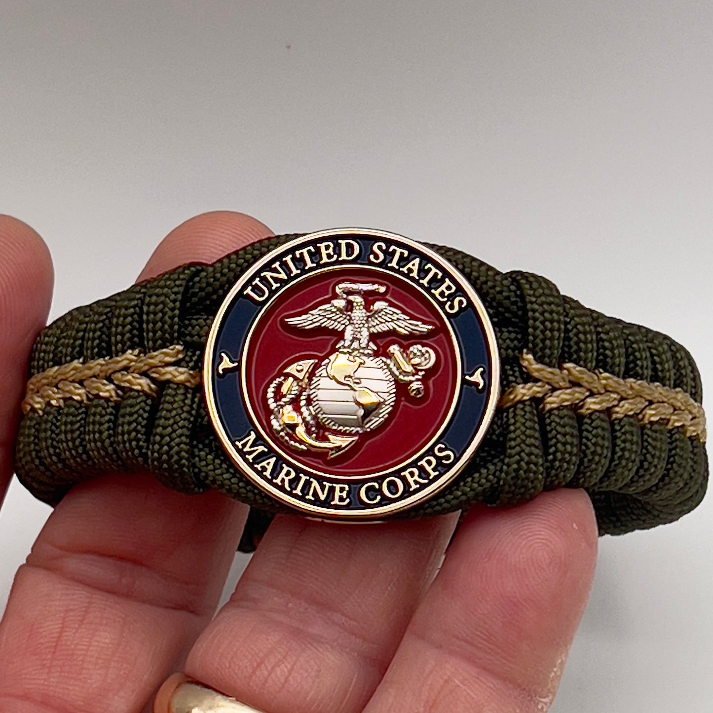 Thick, semi-rigid and comfortable braided United States Marine Corps bracelet featuring a 24K gold and silver plated USMC officer Eagle Globe and Anchor medallion, a gold Cobra style tactical buckle and woven with olive drab 550 and gold micro paracord.