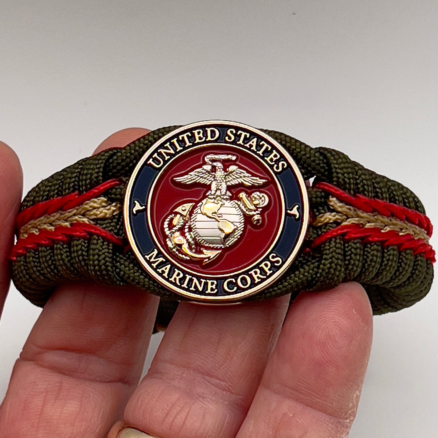 Thick, semi-rigid and comfortable braided United States Marine Corps bracelet featuring a 24K gold and silver plated USMC officer Eagle Globe and Anchor medallion, a gold Cobra style tactical buckle and woven with olive drab 550 and gold micro paracord.