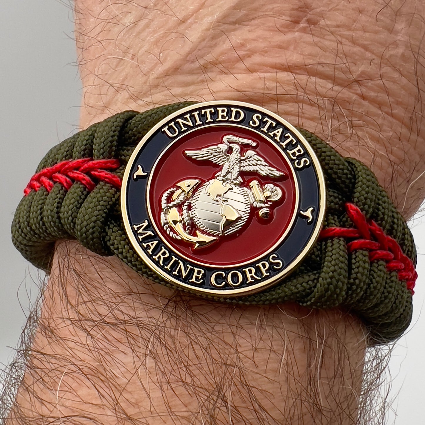 Thick, semi-rigid and comfortable braided United States Marine Corps bracelet featuring a 24K gold and silver plated USMC officer Eagle Globe and Anchor medallion, a gold Cobra style tactical buckle and woven with olive drab 550 and Imperial red micro paracord.