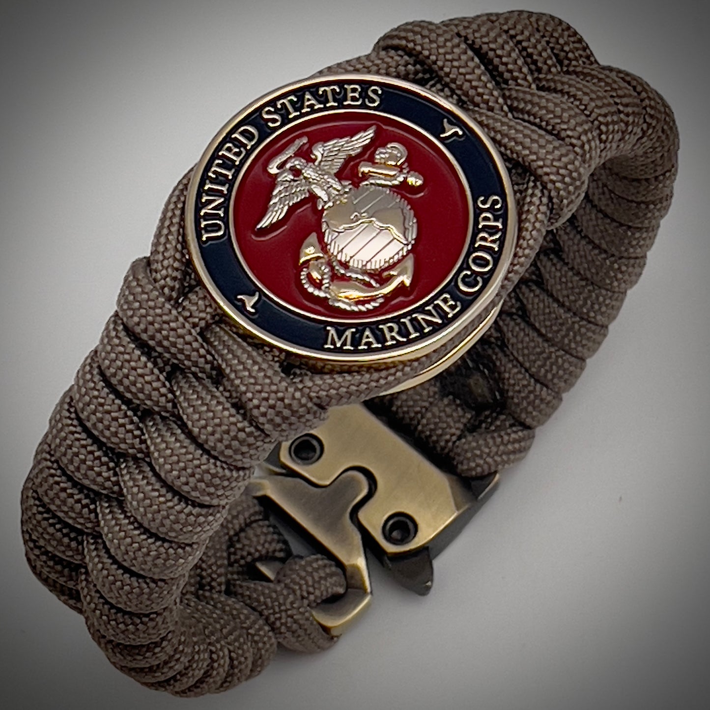 Thick, semi-rigid and comfortable braided United States Marine Corps bracelet featuring a 24K gold and silver plated USMC officer Eagle Globe and Anchor medallion, a gold Cobra style tactical buckle and woven with tan 550 paracord.