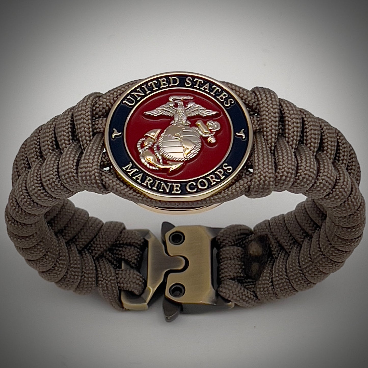 Thick, semi-rigid and comfortable braided United States Marine Corps bracelet featuring a 24K gold and silver plated USMC officer Eagle Globe and Anchor medallion, a gold Cobra style tactical buckle and woven with tan 550 paracord.