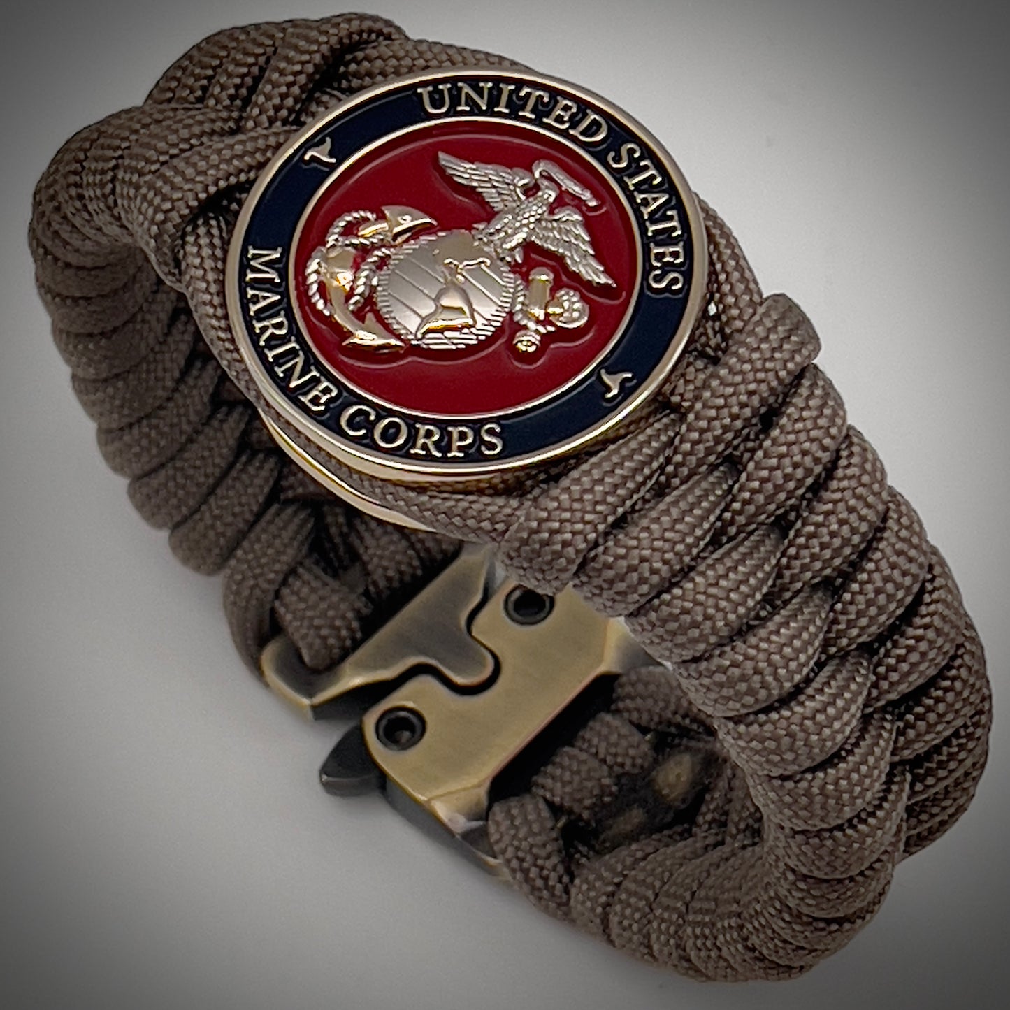 Thick, semi-rigid and comfortable braided United States Marine Corps bracelet featuring a 24K gold and silver plated USMC officer Eagle Globe and Anchor medallion, a gold Cobra style tactical buckle and woven with tan 550 paracord.