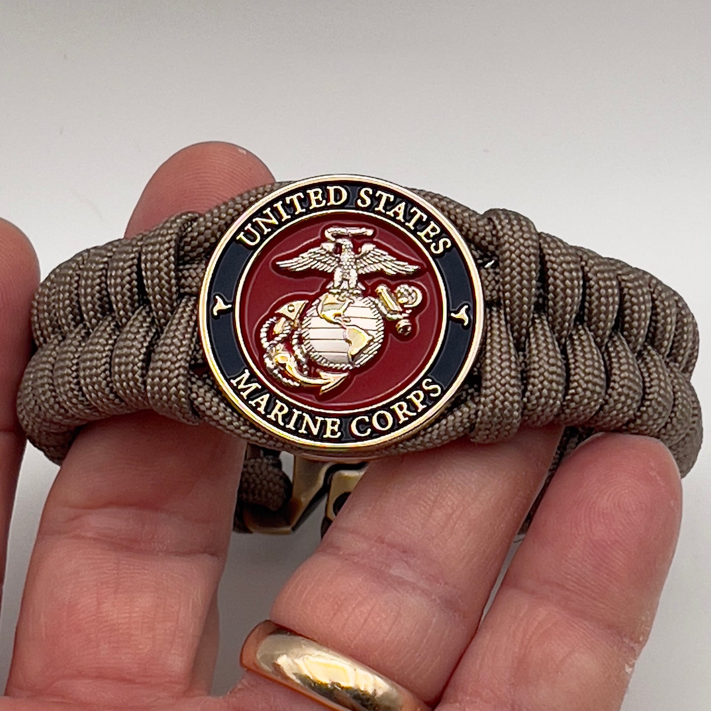 Thick, semi-rigid and comfortable braided United States Marine Corps bracelet featuring a 24K gold and silver plated USMC officer Eagle Globe and Anchor medallion, a gold Cobra style tactical buckle and woven with tan 550 paracord.