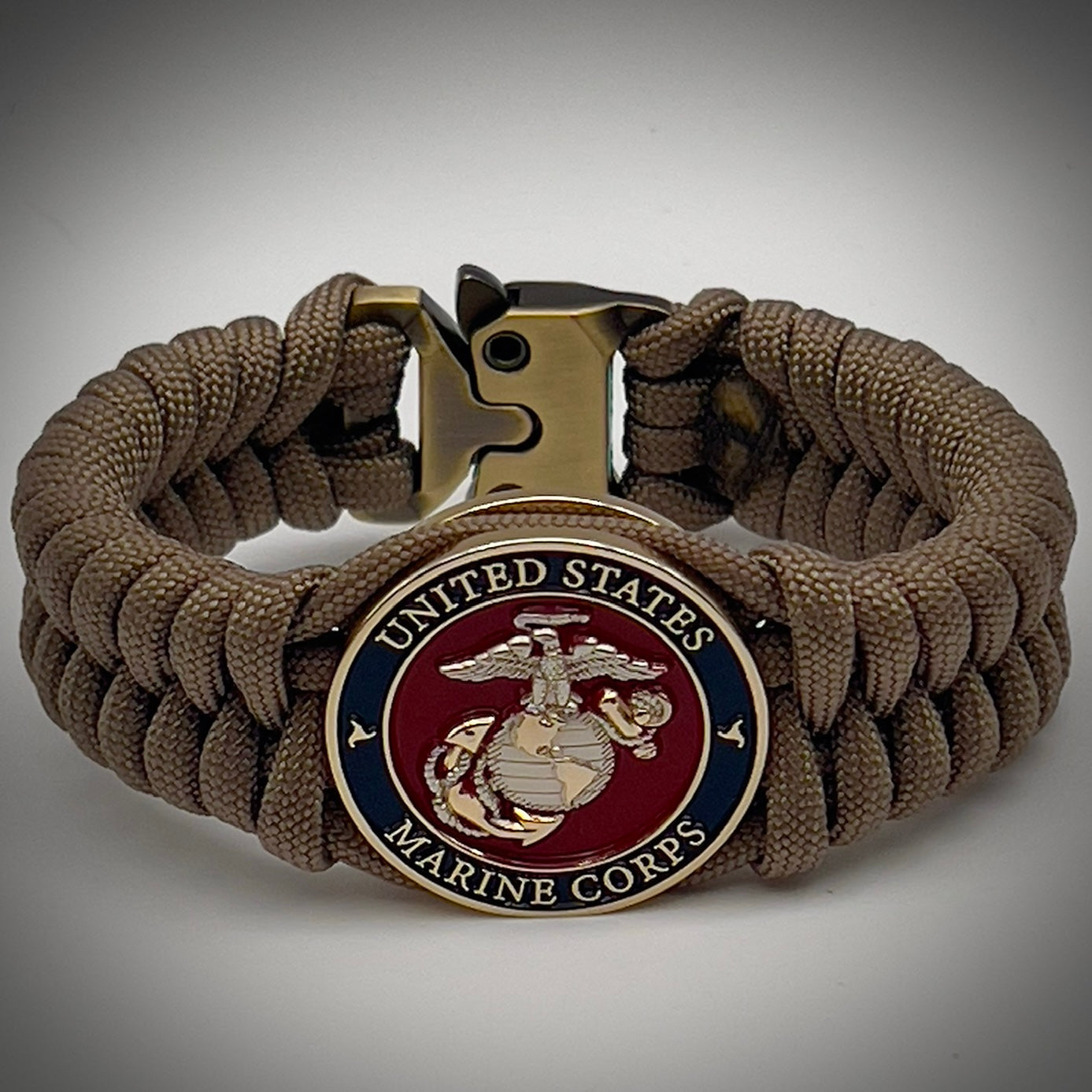 Thick, semi-rigid and comfortable braided United States Marine Corps bracelet featuring a 24K gold and silver plated USMC officer Eagle Globe and Anchor medallion, a gold Cobra style tactical buckle and woven with tan 550 paracord.