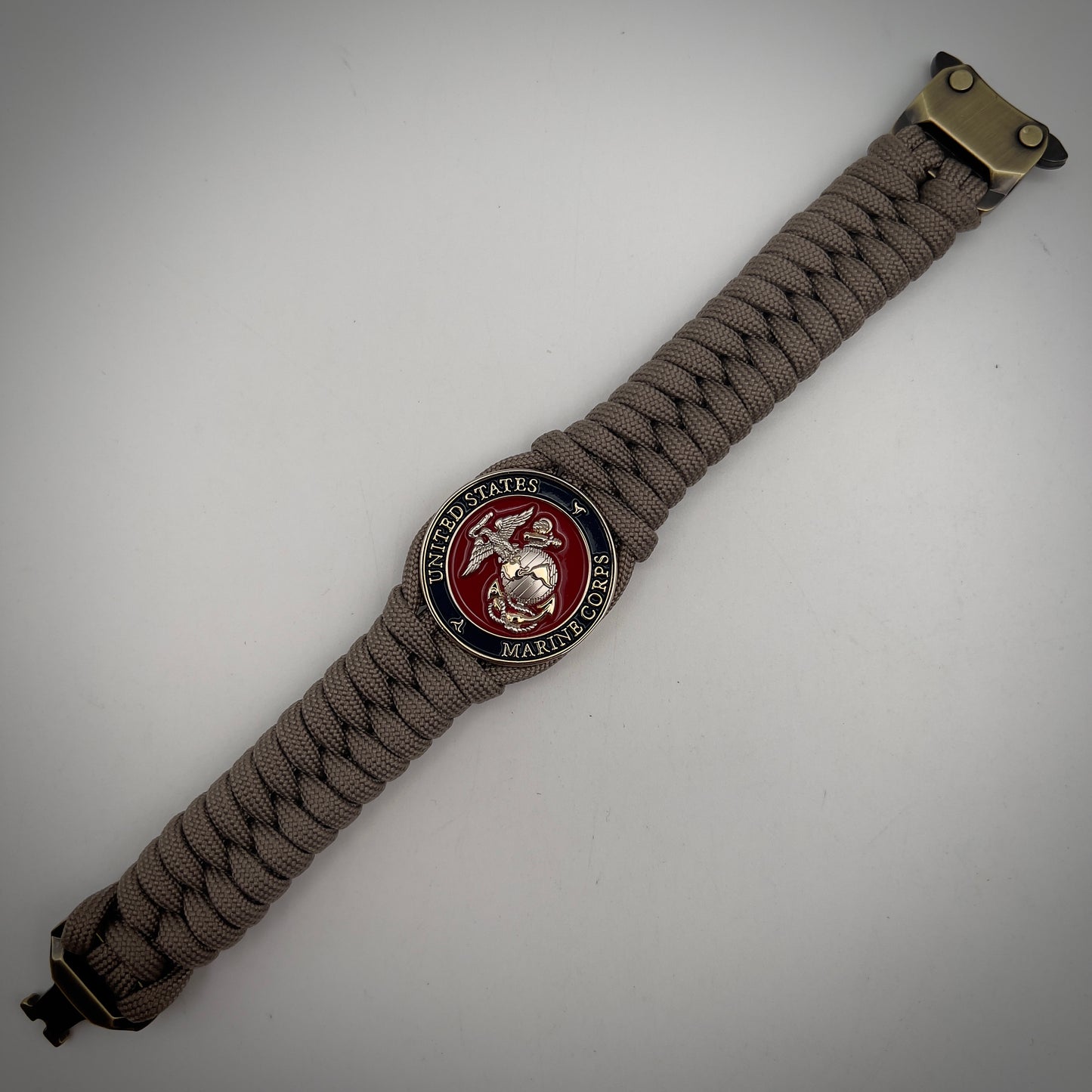 Thick, semi-rigid and comfortable braided United States Marine Corps bracelet featuring a 24K gold and silver plated USMC officer Eagle Globe and Anchor medallion, a gold Cobra style tactical buckle and woven with tan 550 paracord.