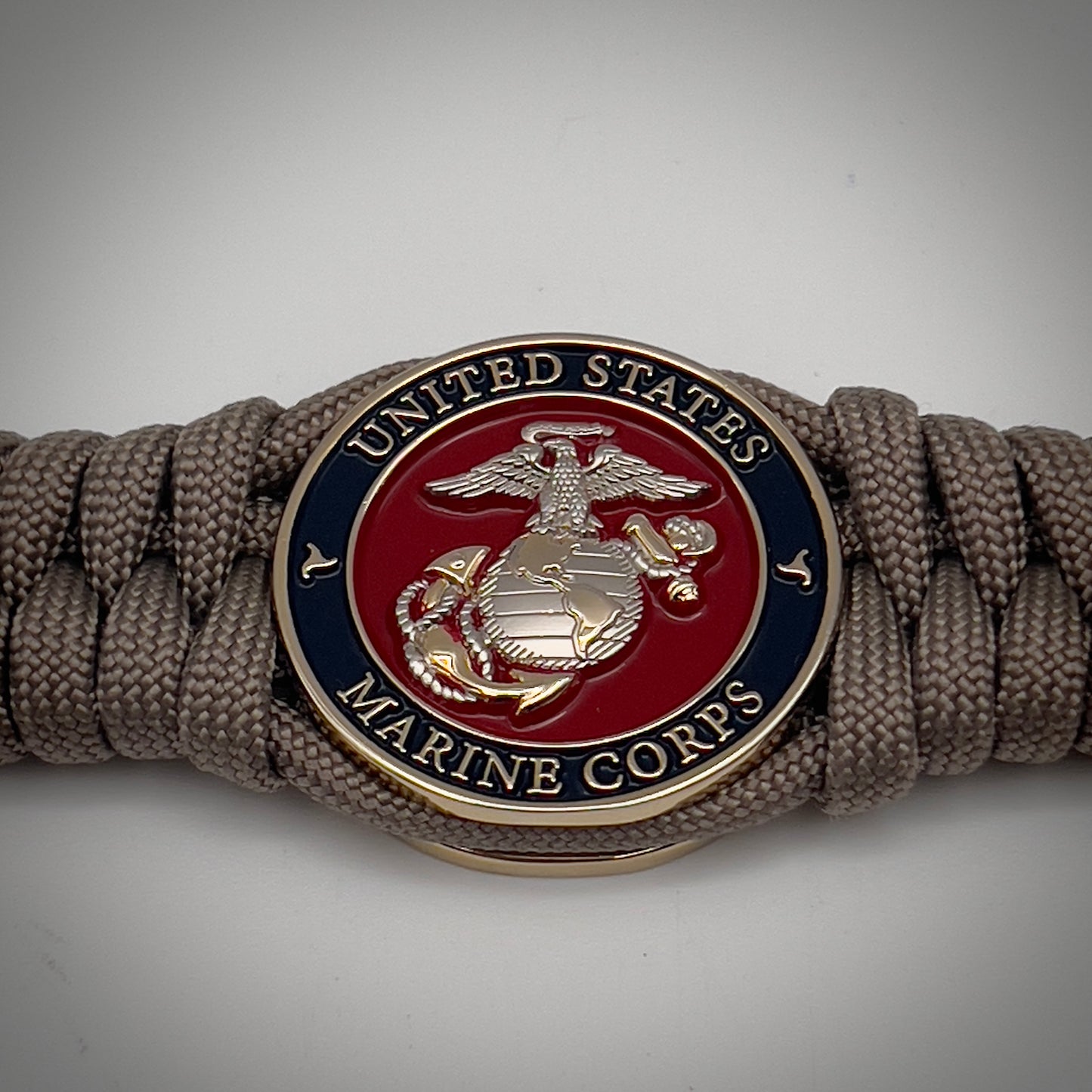 Thick, semi-rigid and comfortable braided United States Marine Corps bracelet featuring a 24K gold and silver plated USMC officer Eagle Globe and Anchor medallion, a gold Cobra style tactical buckle and woven with tan 550 paracord.