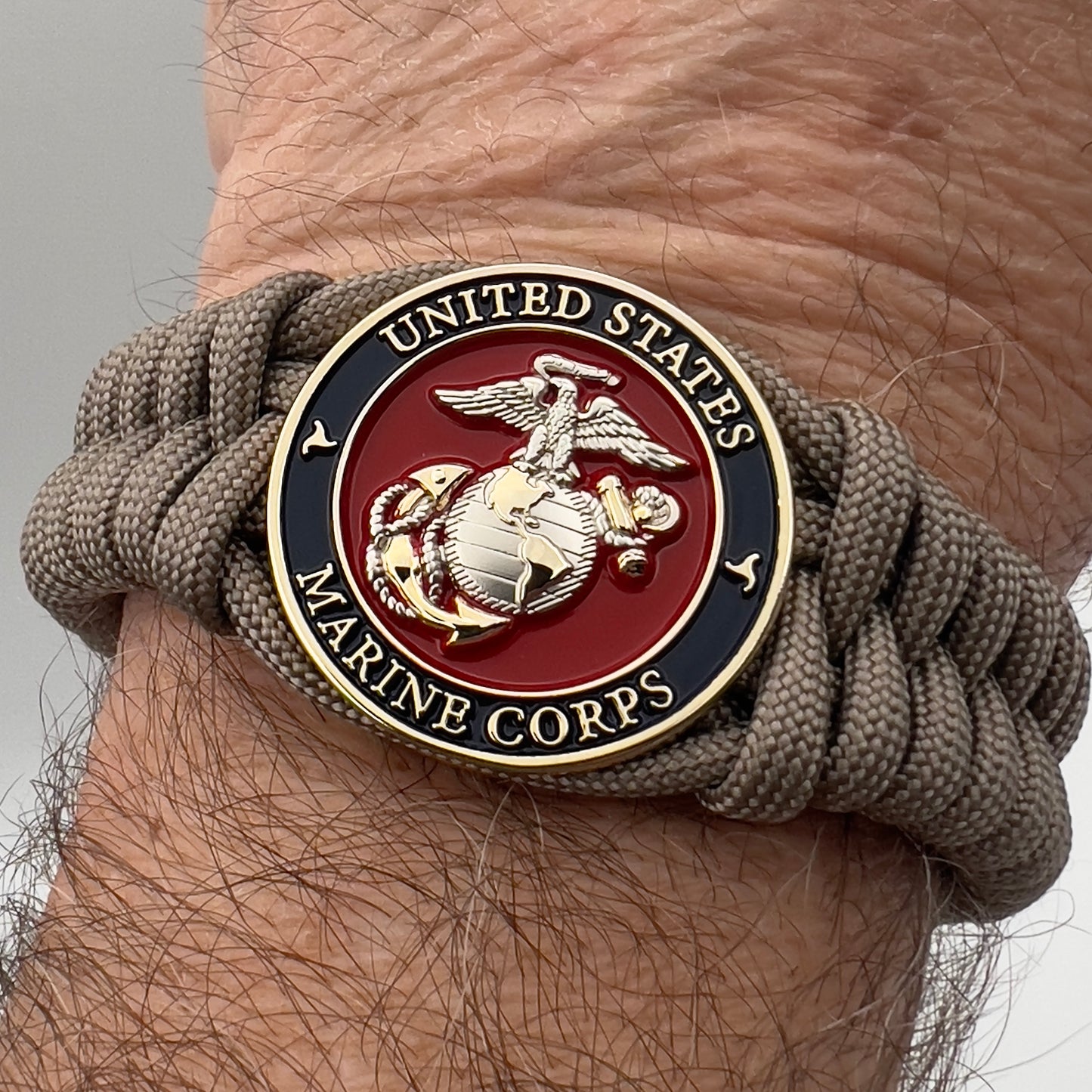 Thick, semi-rigid and comfortable braided United States Marine Corps bracelet featuring a 24K gold and silver plated USMC officer Eagle Globe and Anchor medallion, a gold Cobra style tactical buckle and woven with tan 550 paracord.