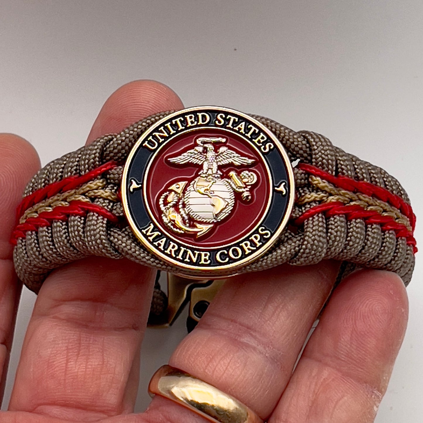 Thick and comfortable braided United States Marine Corps bracelet featuring a 24K gold and silver plated USMC officer Eagle Globe and Anchor medallion, a Cobra style tactical buckle and woven with tan 550, Imperial red and gold micro paracord.