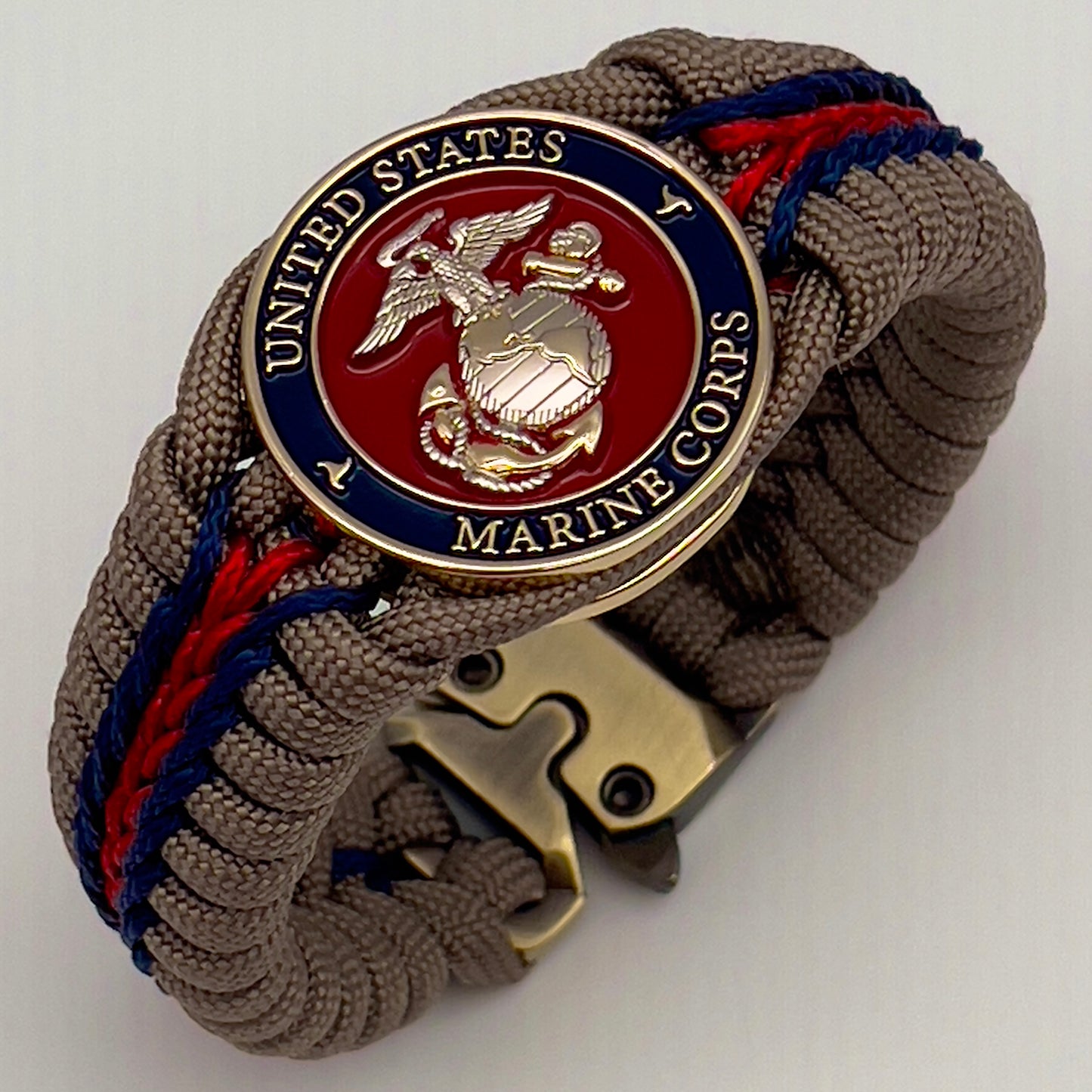Thick, semi-rigid and comfortable braided United States Marine Corps bracelet featuring a 24K gold and silver plated USMC officer Eagle Globe and Anchor medallion, a gold Cobra style tactical buckle and woven with tan 550 paracord and Imperial red and gold micro cord.