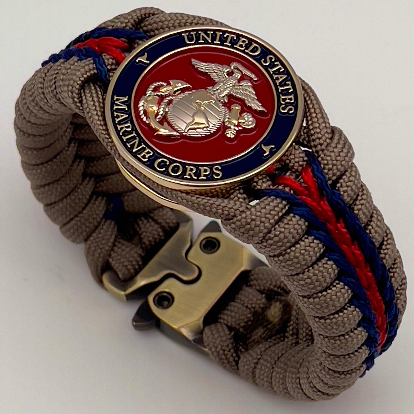 Thick, semi-rigid and comfortable braided United States Marine Corps bracelet featuring a 24K gold and silver plated USMC officer Eagle Globe and Anchor medallion, a gold Cobra style tactical buckle and woven with tan 550 paracord and Imperial red and gold micro cord.