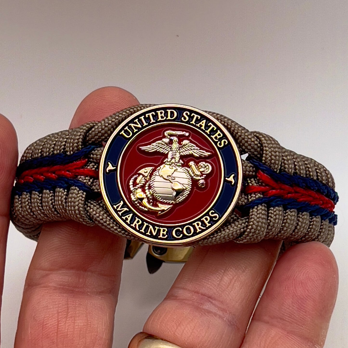 Thick, semi-rigid and comfortable braided United States Marine Corps bracelet featuring a 24K gold and silver plated USMC officer Eagle Globe and Anchor medallion, a gold Cobra style tactical buckle and woven with tan 550 paracord and Imperial red and gold micro cord.