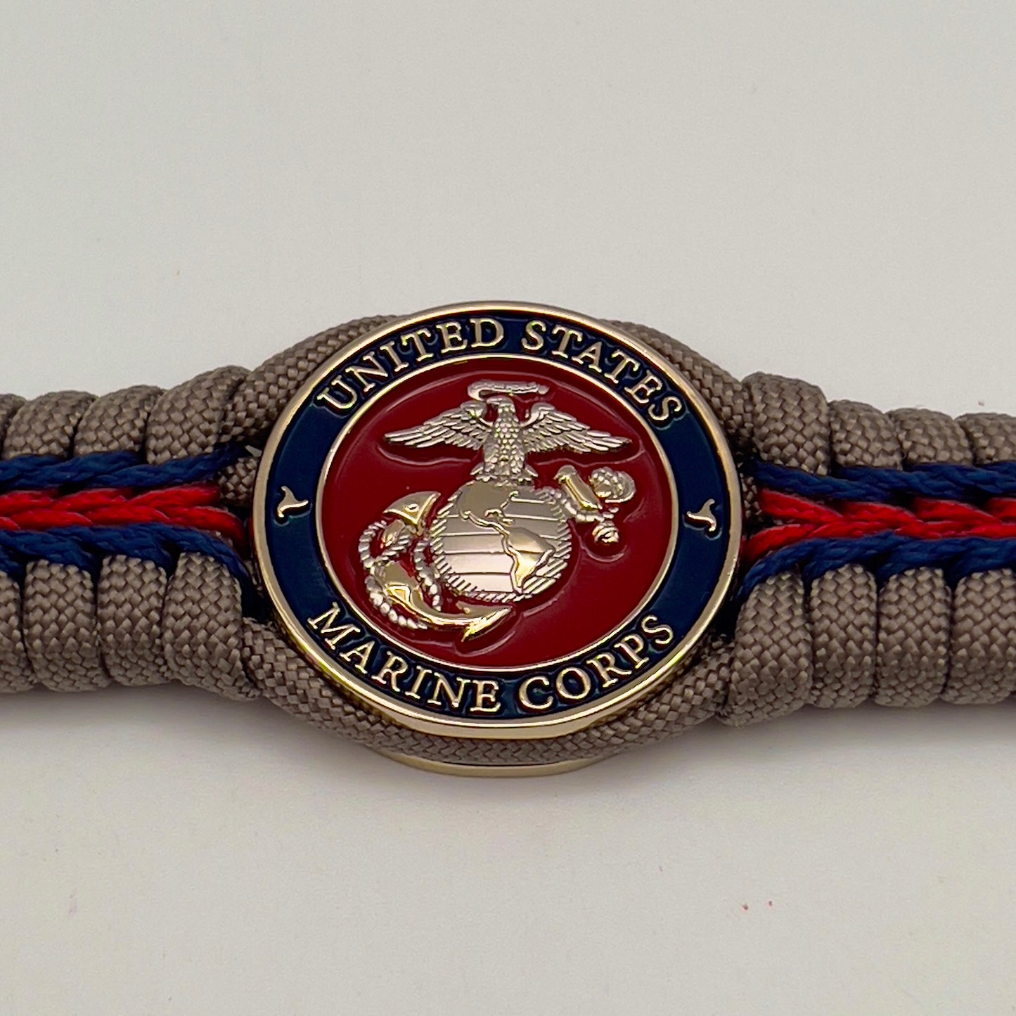 Thick, semi-rigid and comfortable braided United States Marine Corps bracelet featuring a 24K gold and silver plated USMC officer Eagle Globe and Anchor medallion, a gold Cobra style tactical buckle and woven with tan 550 paracord and Imperial red and gold micro cord.