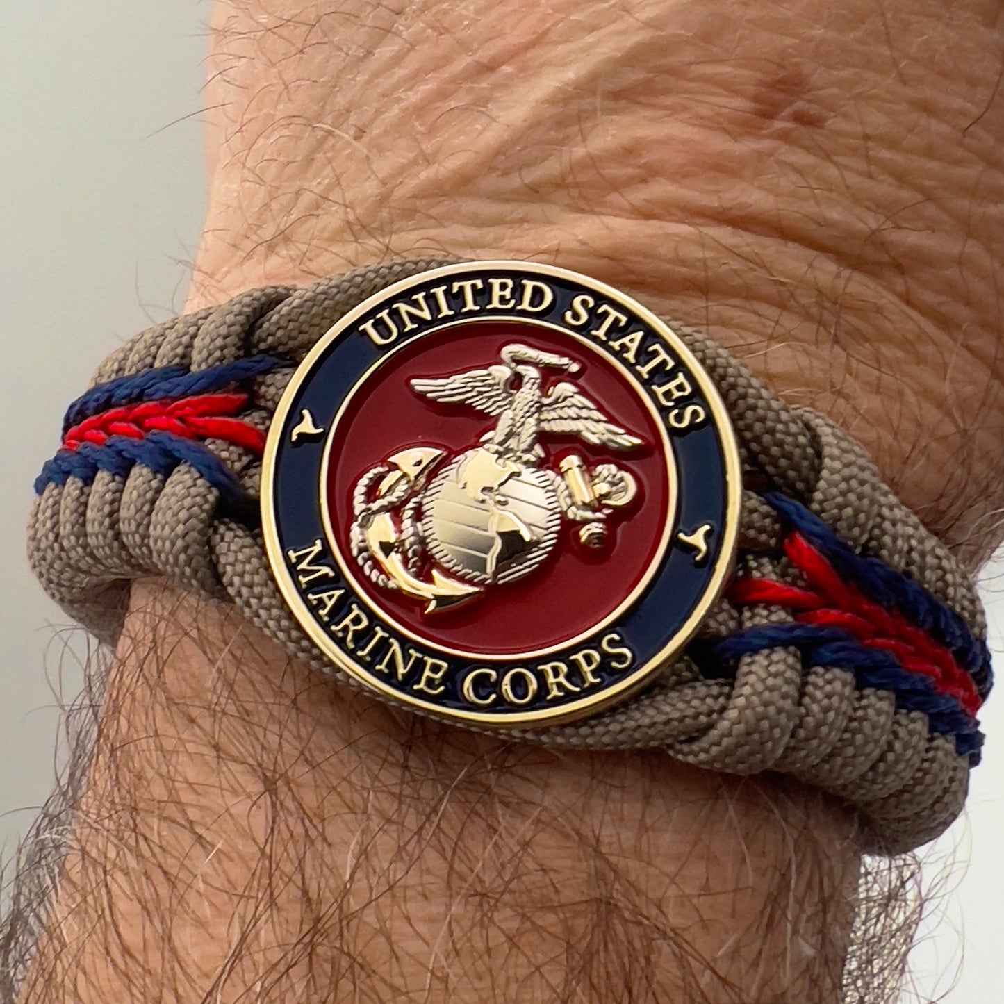 Thick, semi-rigid and comfortable braided United States Marine Corps bracelet featuring a 24K gold and silver plated USMC officer Eagle Globe and Anchor medallion, a gold Cobra style tactical buckle and woven with tan 550 paracord and Imperial red and gold micro cord.