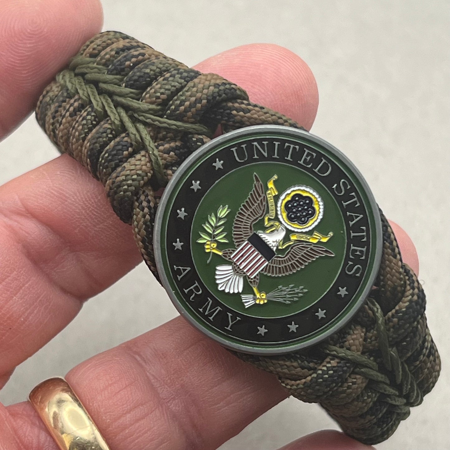 Thick, narrow, rigid and comfortable braided United States Army bracelet featuring an antique silver plated baked enamel hand painted US Army medallion, a black Cobra style tactical buckle and woven with Woodland Camo 550 paracord and Olive Drab micro cord.
