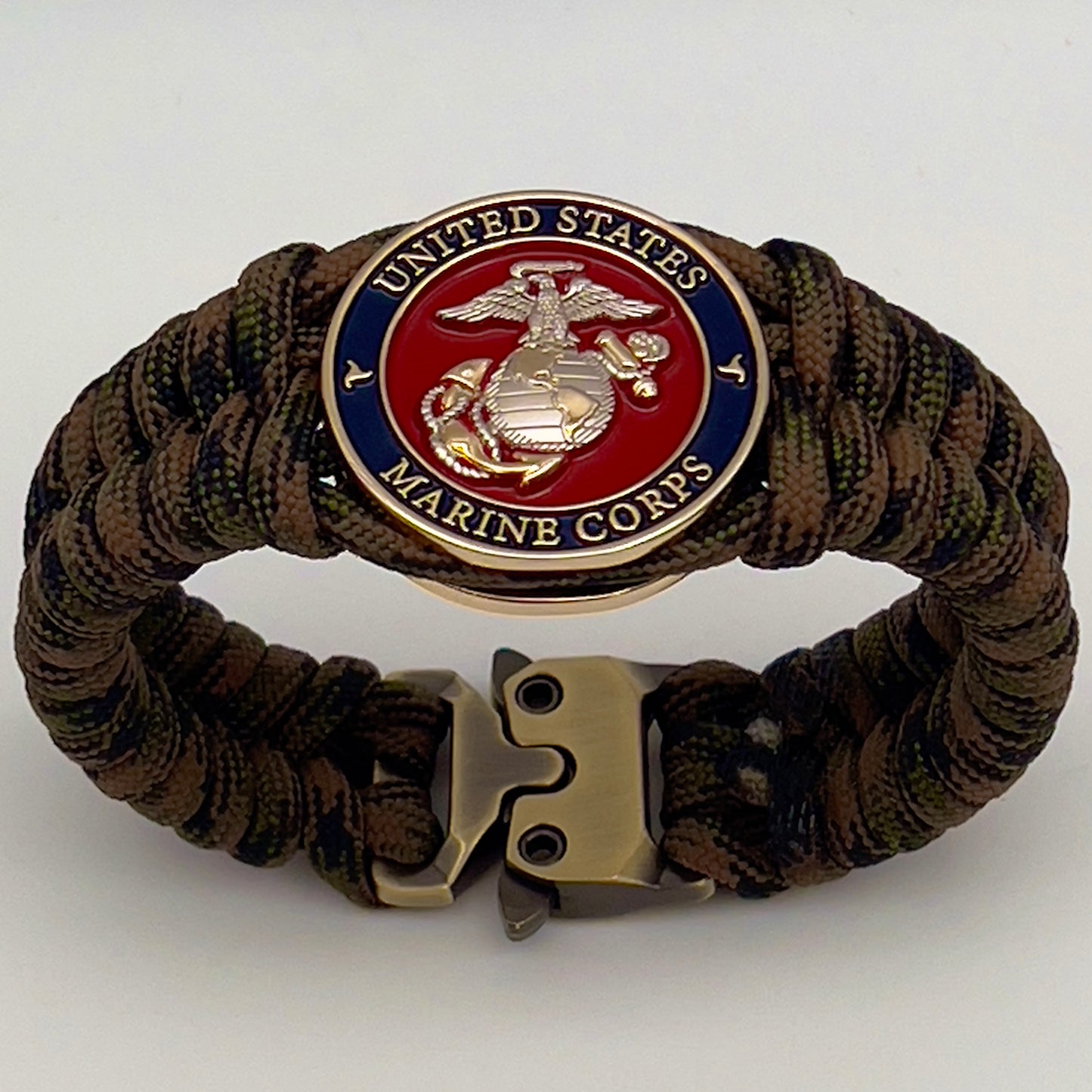 Thick, semi-rigid and comfortable braided United States Marine Corps bracelet featuring a 24K gold and silver plated USMC officer Eagle Globe and Anchor medallion, a gold Cobra style tactical buckle and woven with Woodland Camo 550 paracord.