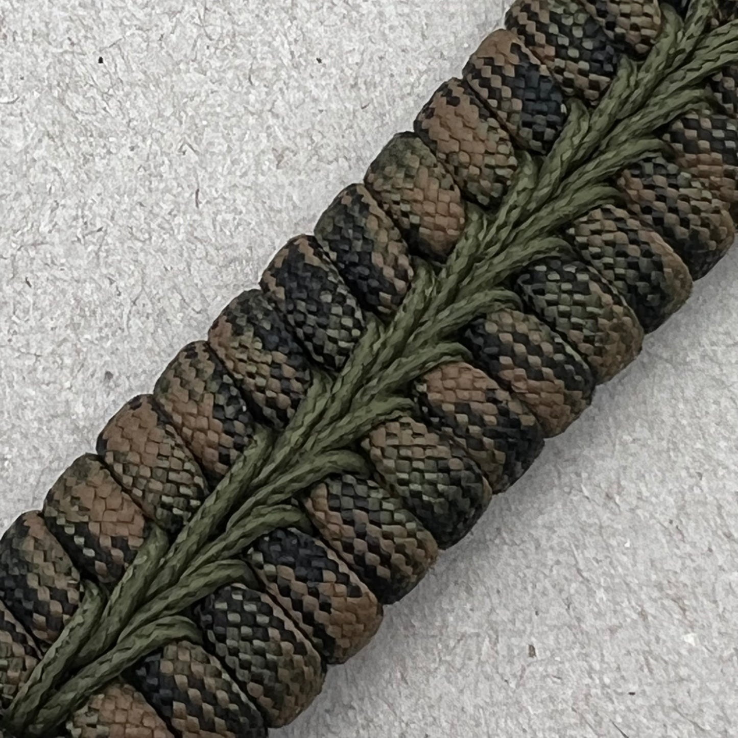 Thick, narrow, rigid and comfortable braided United States Army bracelet featuring an antique silver plated baked enamel hand painted US Army medallion, a black Cobra style tactical buckle and woven with Woodland Camo 550 paracord and Olive Drab micro cord.