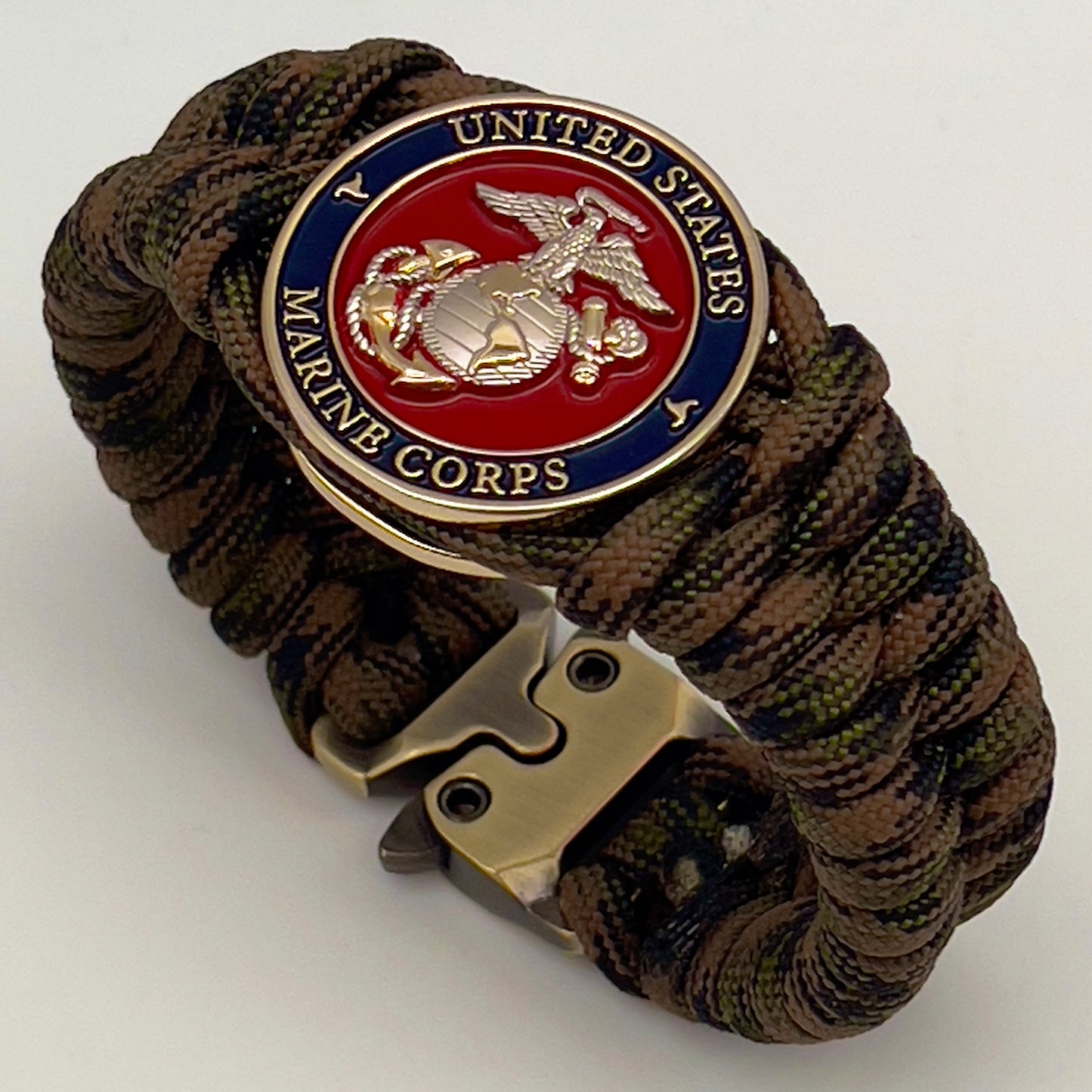 Thick, semi-rigid and comfortable braided United States Marine Corps bracelet featuring a 24K gold and silver plated USMC officer Eagle Globe and Anchor medallion, a gold Cobra style tactical buckle and woven with Woodland Camo 550 paracord.