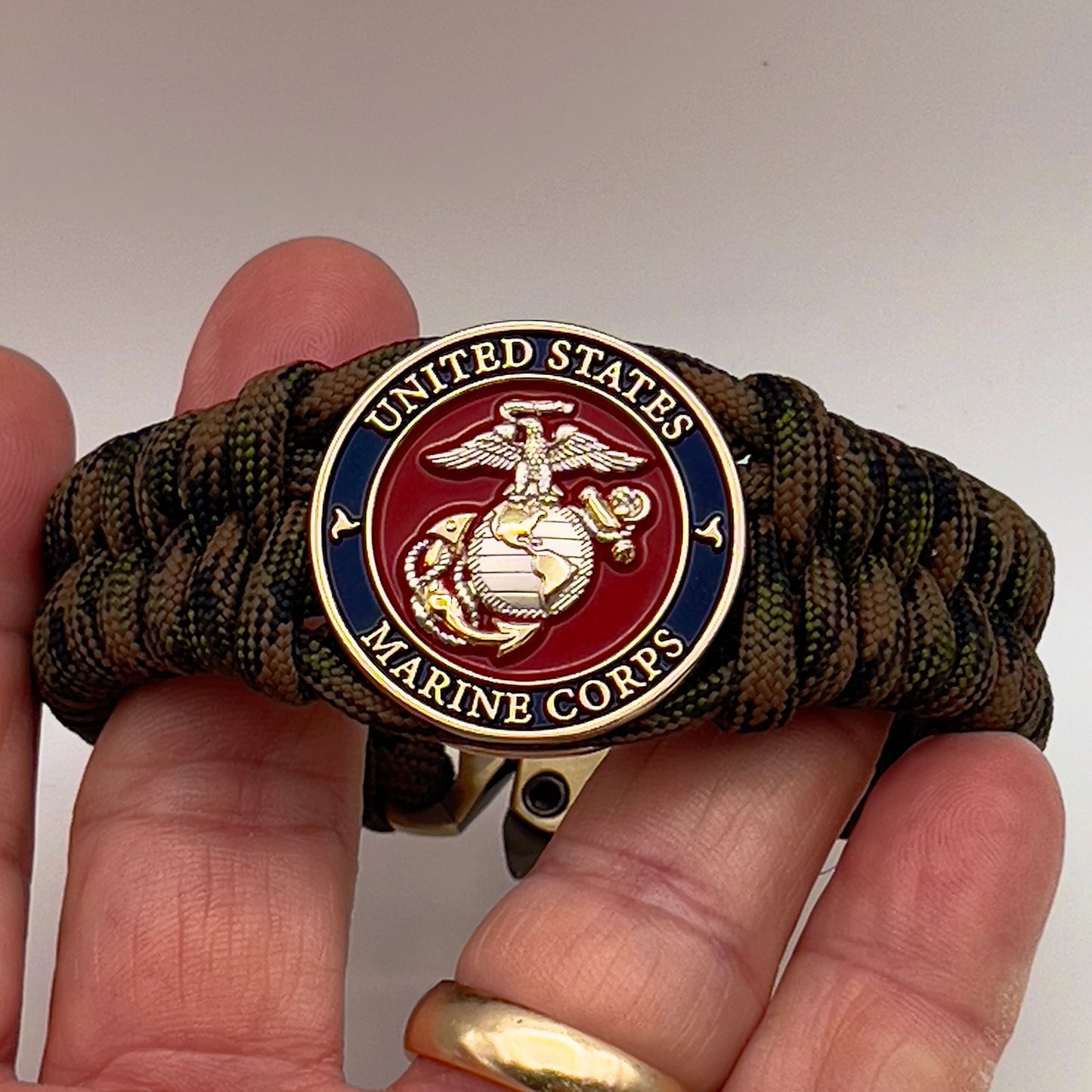 Thick, semi-rigid and comfortable braided United States Marine Corps bracelet featuring a 24K gold and silver plated USMC officer Eagle Globe and Anchor medallion, a gold Cobra style tactical buckle and woven with Woodland Camo 550 paracord.