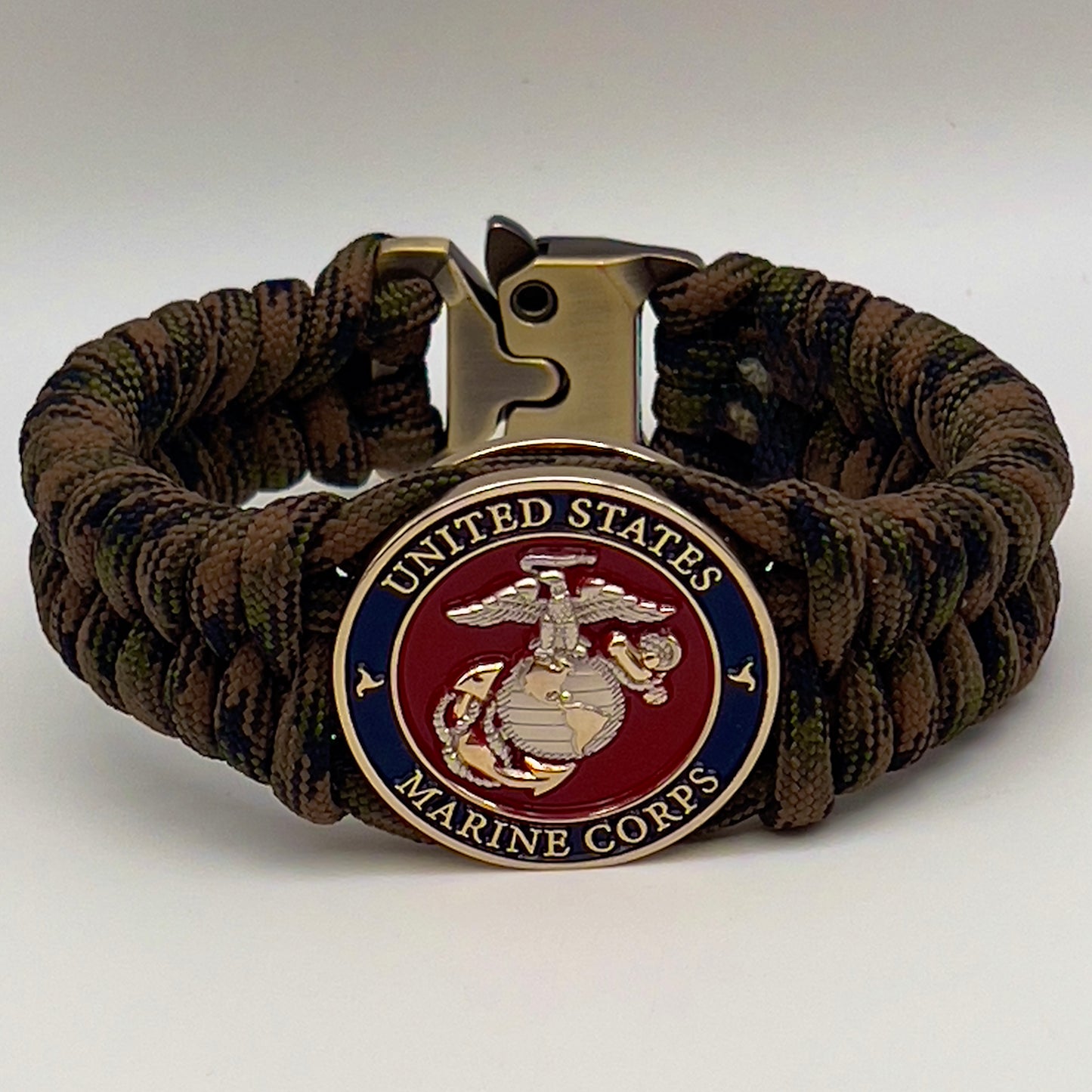 Thick, semi-rigid and comfortable braided United States Marine Corps bracelet featuring a 24K gold and silver plated USMC officer Eagle Globe and Anchor medallion, a gold Cobra style tactical buckle and woven with Woodland Camo 550 paracord.