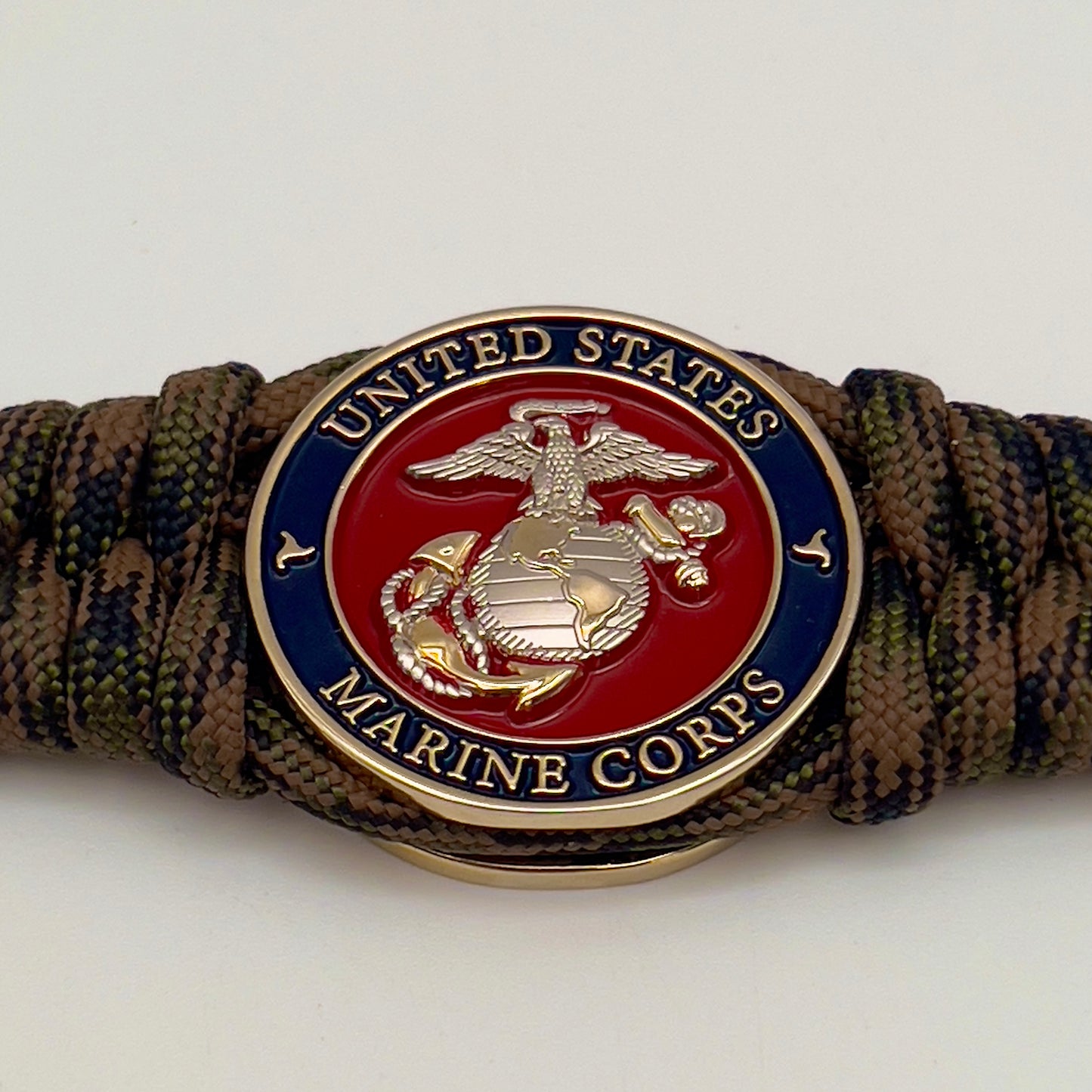 Thick, semi-rigid and comfortable braided United States Marine Corps bracelet featuring a 24K gold and silver plated USMC officer Eagle Globe and Anchor medallion, a gold Cobra style tactical buckle and woven with Woodland Camo 550 paracord.