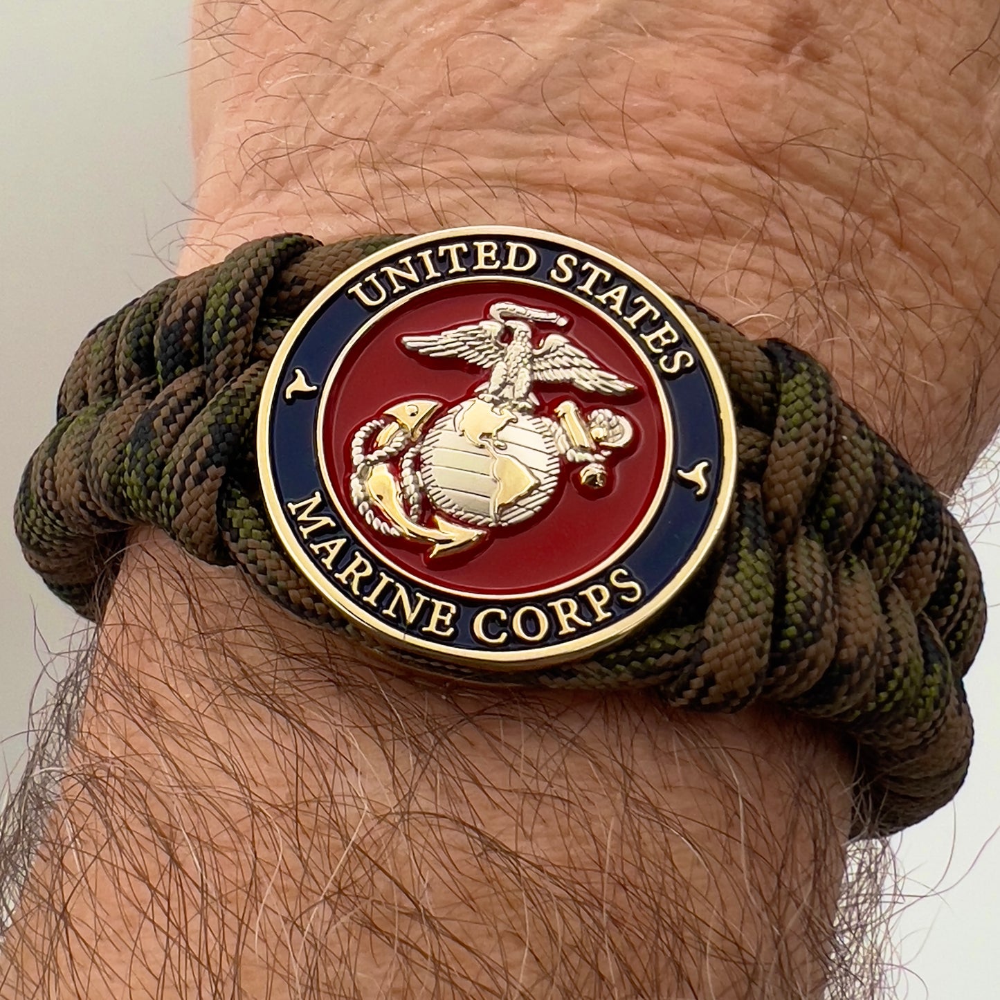 Thick, semi-rigid and comfortable braided United States Marine Corps bracelet featuring a 24K gold and silver plated USMC officer Eagle Globe and Anchor medallion, a gold Cobra style tactical buckle and woven with Woodland Camo 550 paracord.