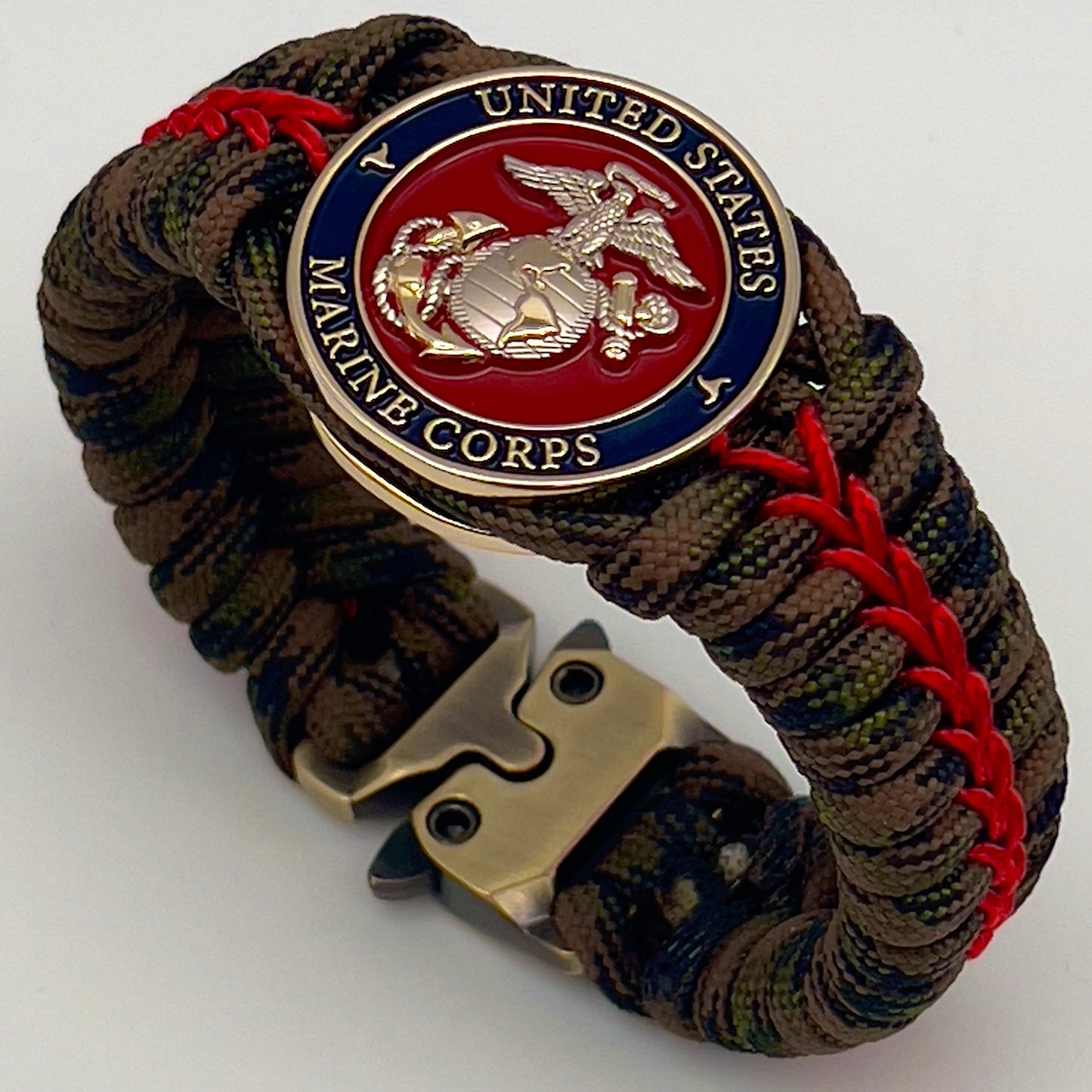 Thick, semi-rigid and comfortable braided United States Marine Corps bracelet featuring a 24K gold and silver plated USMC officer Eagle Globe and Anchor medallion, a gold Cobra style tactical buckle and woven with Woodland Camo 550 paracord and Imperial Red micro cord.