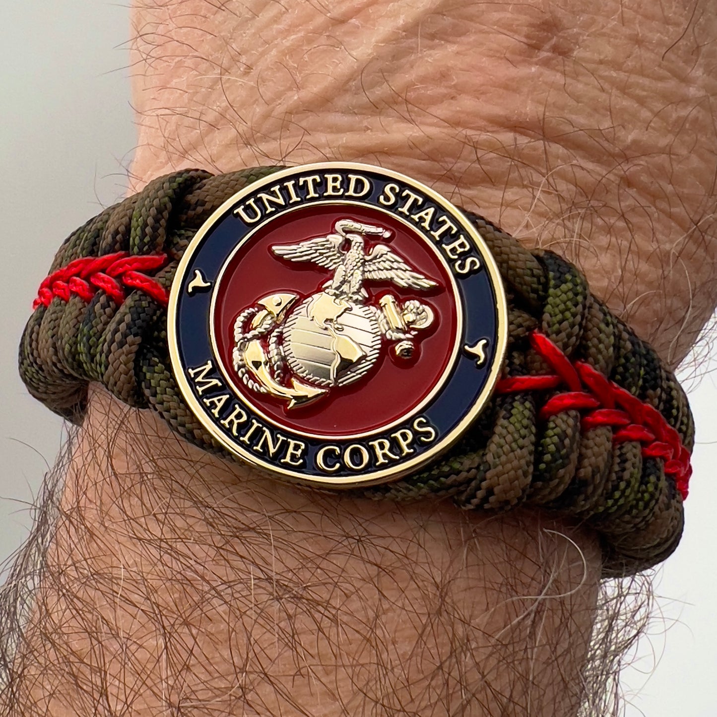 Thick, semi-rigid and comfortable braided United States Marine Corps bracelet featuring a 24K gold and silver plated USMC officer Eagle Globe and Anchor medallion, a gold Cobra style tactical buckle and woven with Woodland Camo 550 paracord and Imperial Red micro cord.