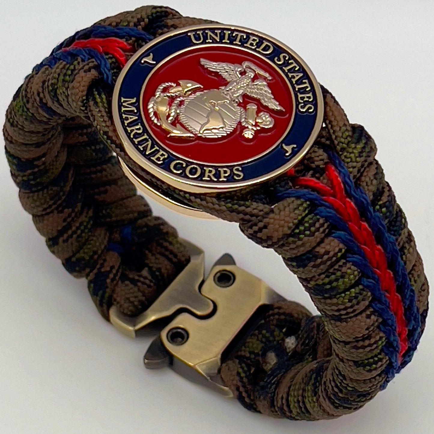 Thick, semi-rigid and comfortable braided United States Marine Corps bracelet featuring a 24K gold and silver plated USMC officer Eagle Globe and Anchor medallion, a gold Cobra style tactical buckle and woven with Woodland Camo 550 paracord and Imperial Red and Navy Blue micro cord.