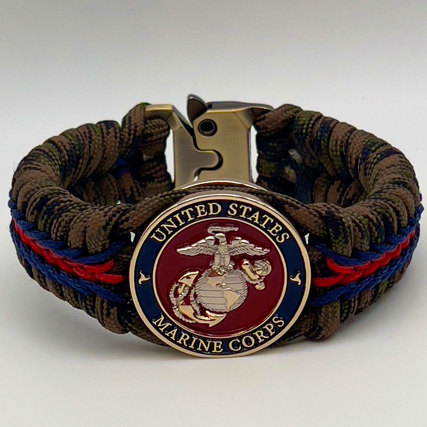Thick, semi-rigid and comfortable braided United States Marine Corps bracelet featuring a 24K gold and silver plated USMC officer Eagle Globe and Anchor medallion, a gold Cobra style tactical buckle and woven with Woodland Camo 550 paracord and Imperial Red and Navy Blue micro cord.