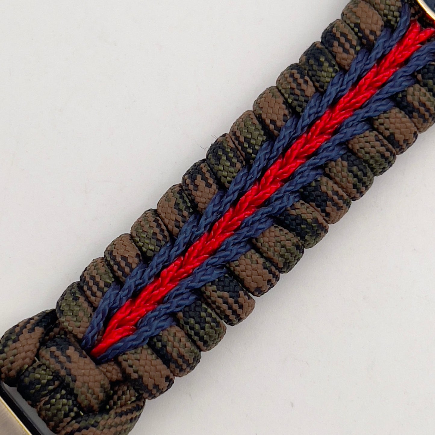 Thick, semi-rigid and comfortable braided United States Marine Corps bracelet featuring a 24K gold and silver plated USMC officer Eagle Globe and Anchor medallion, a gold Cobra style tactical buckle and woven with Woodland Camo 550 paracord and Imperial Red and Navy Blue micro cord.