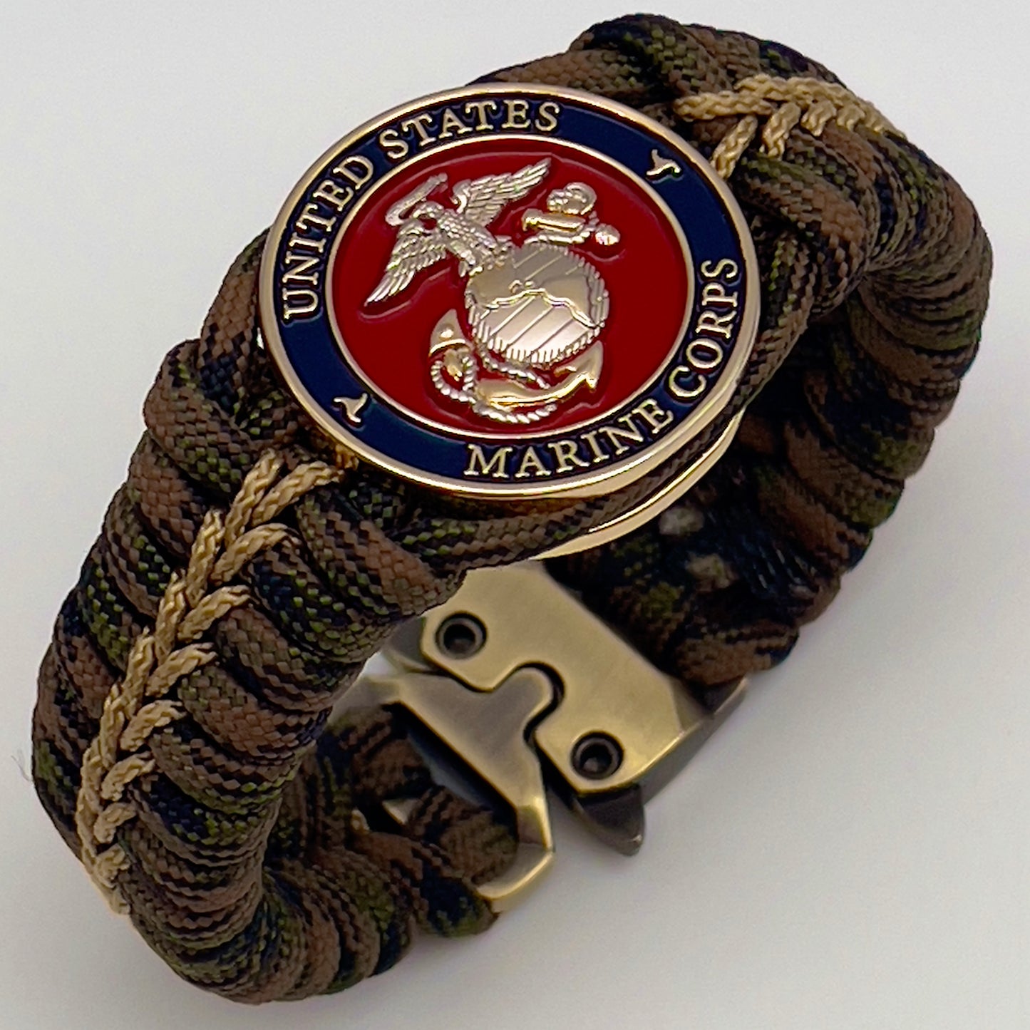 Thick, semi-rigid and comfortable braided United States Marine Corps bracelet featuring a 24K gold and silver plated USMC officer Eagle Globe and Anchor medallion, a gold Cobra style tactical buckle and woven with Woodland Camo 550 paracord and gold micro cord.