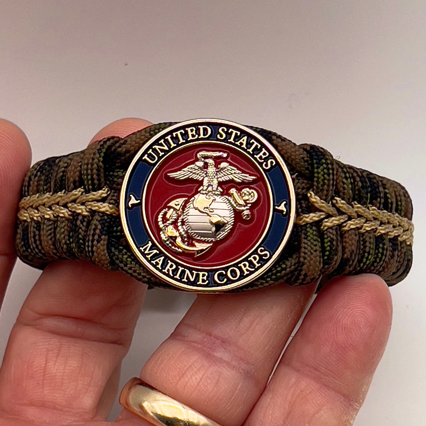 Thick, semi-rigid and comfortable braided United States Marine Corps bracelet featuring a 24K gold and silver plated USMC officer Eagle Globe and Anchor medallion, a gold Cobra style tactical buckle and woven with Woodland Camo 550 paracord and gold micro cord.