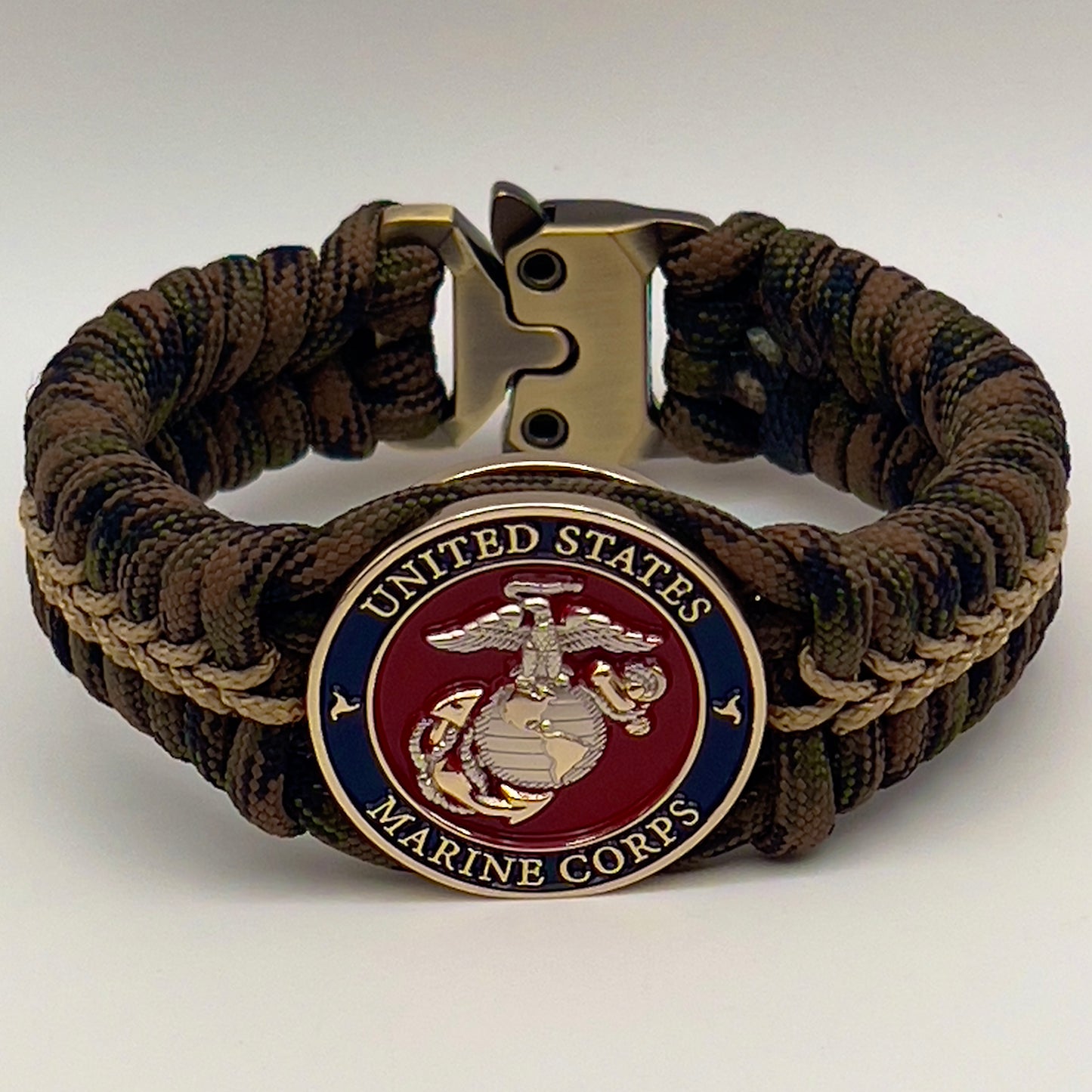 Thick, semi-rigid and comfortable braided United States Marine Corps bracelet featuring a 24K gold and silver plated USMC officer Eagle Globe and Anchor medallion, a gold Cobra style tactical buckle and woven with Woodland Camo 550 paracord and gold micro cord.
